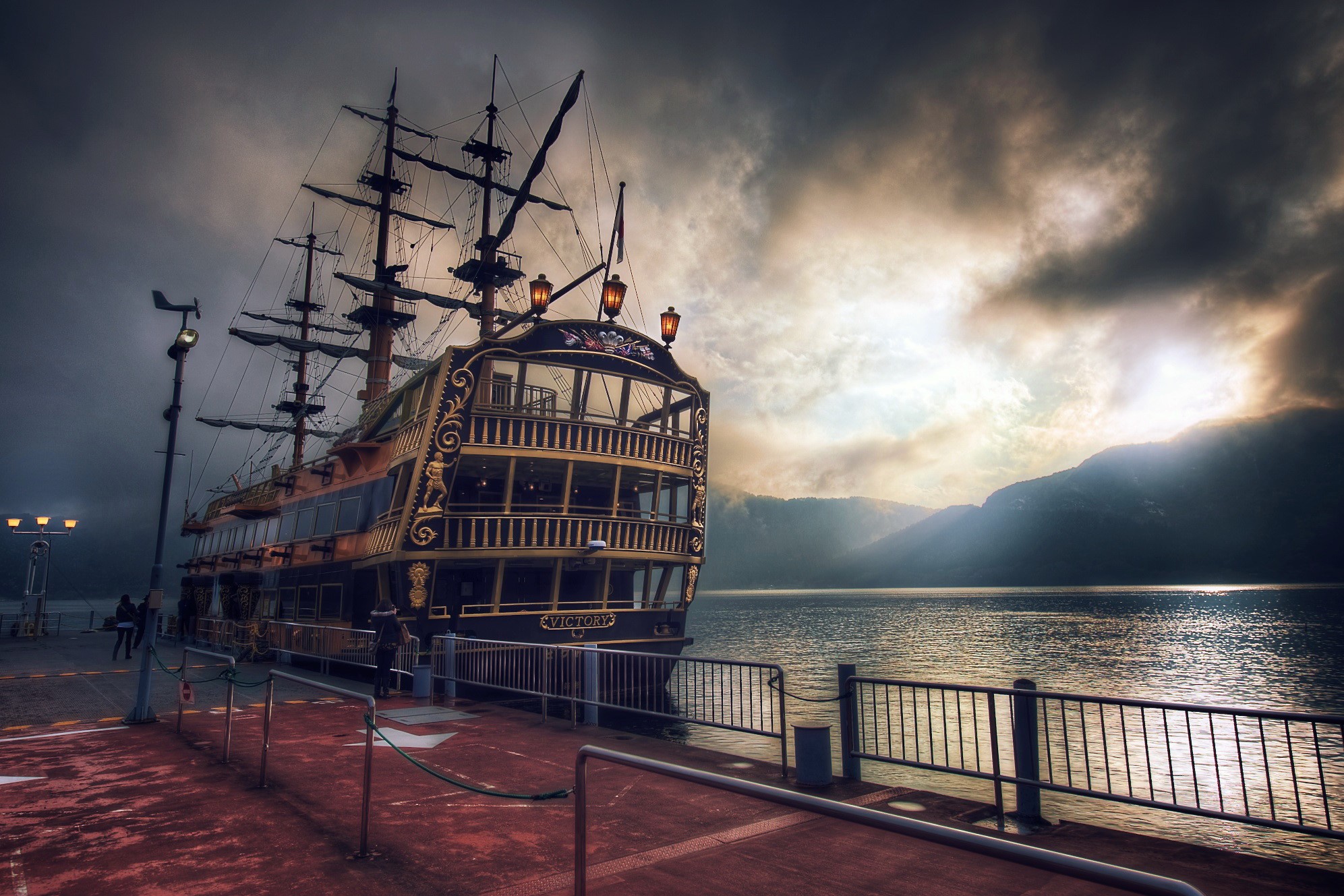 Pirate ship docked by a lake with mountains in the background HD Wallpaper