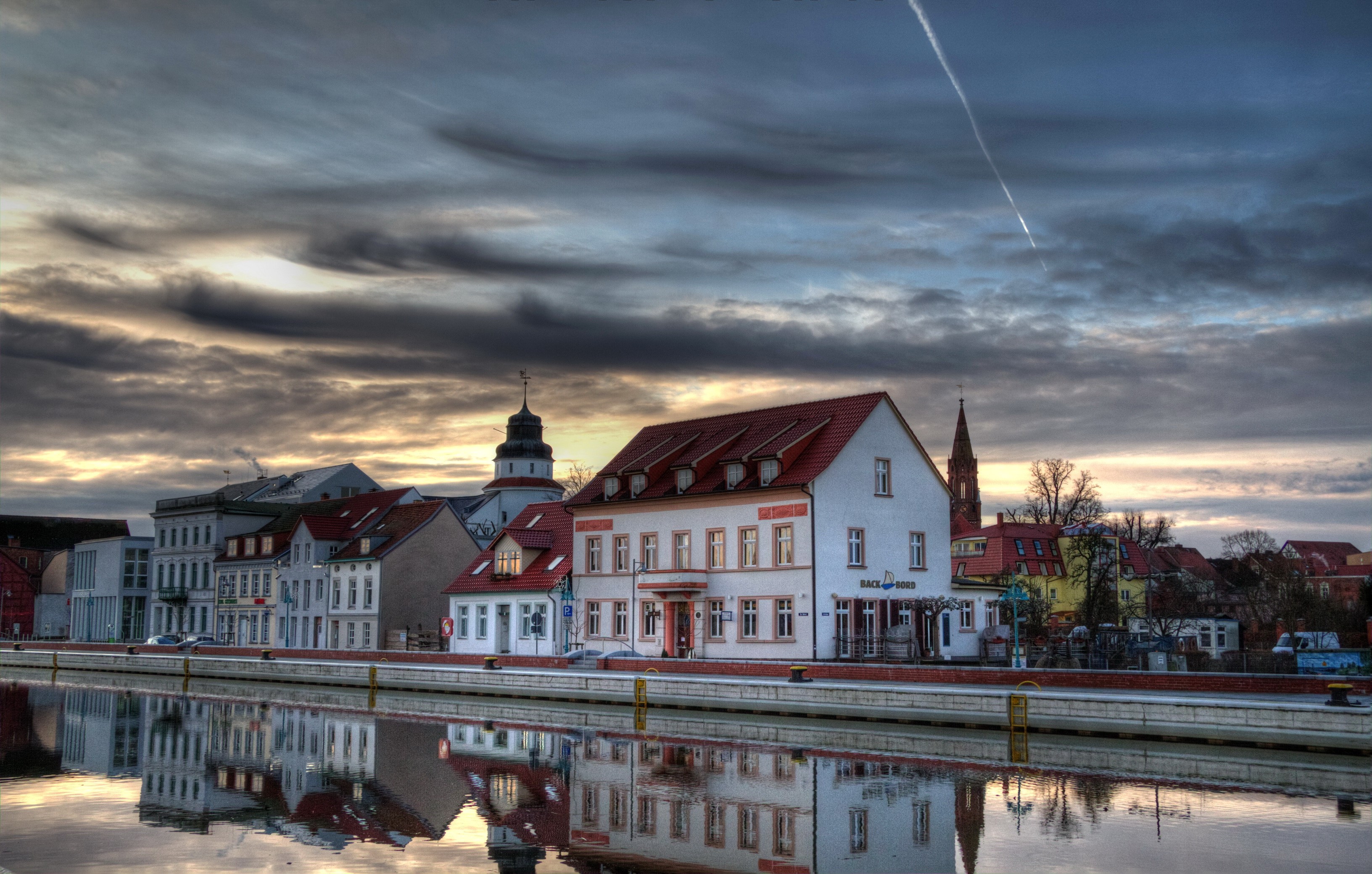 Buildings reflected in a river under a cloudy sky HD Wallpaper
