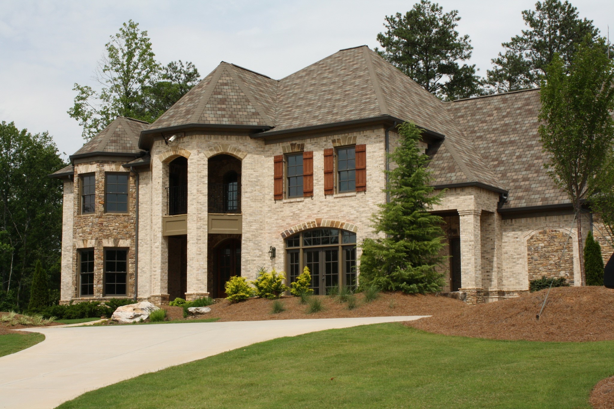 Large brick and stone mansion with arched windows and a circular driveway HD Wallpaper