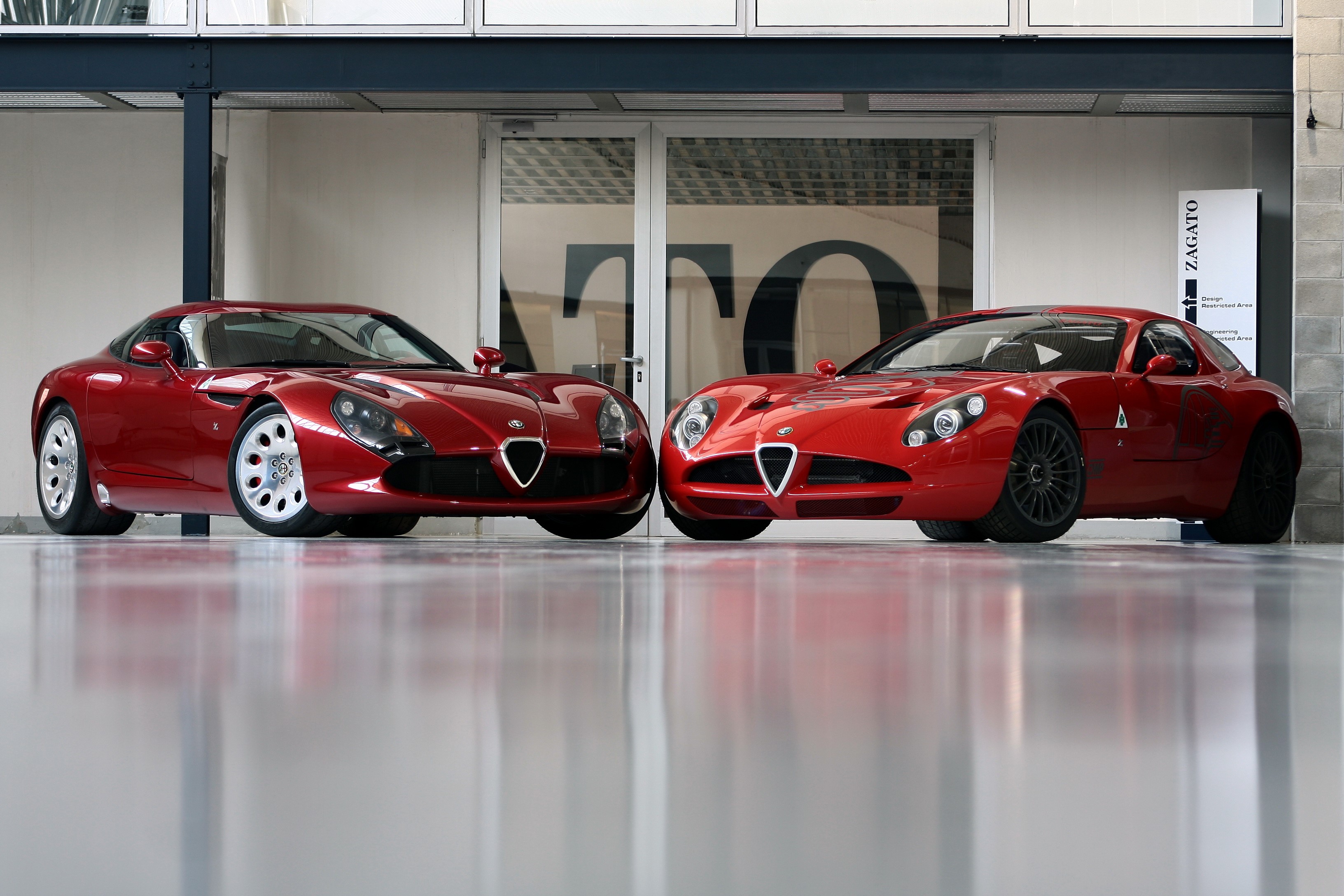 Two red Alfa Romeo cars parked indoors HD Wallpaper