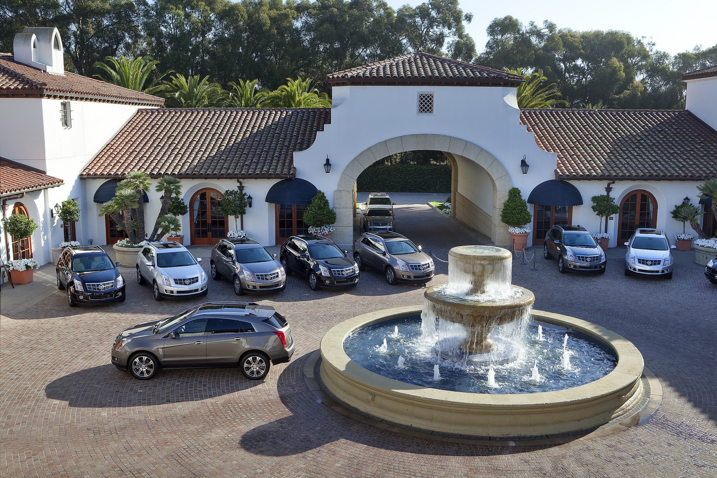 Cadillac SRX SUVs parked at a resort with a fountain HD Wallpaper