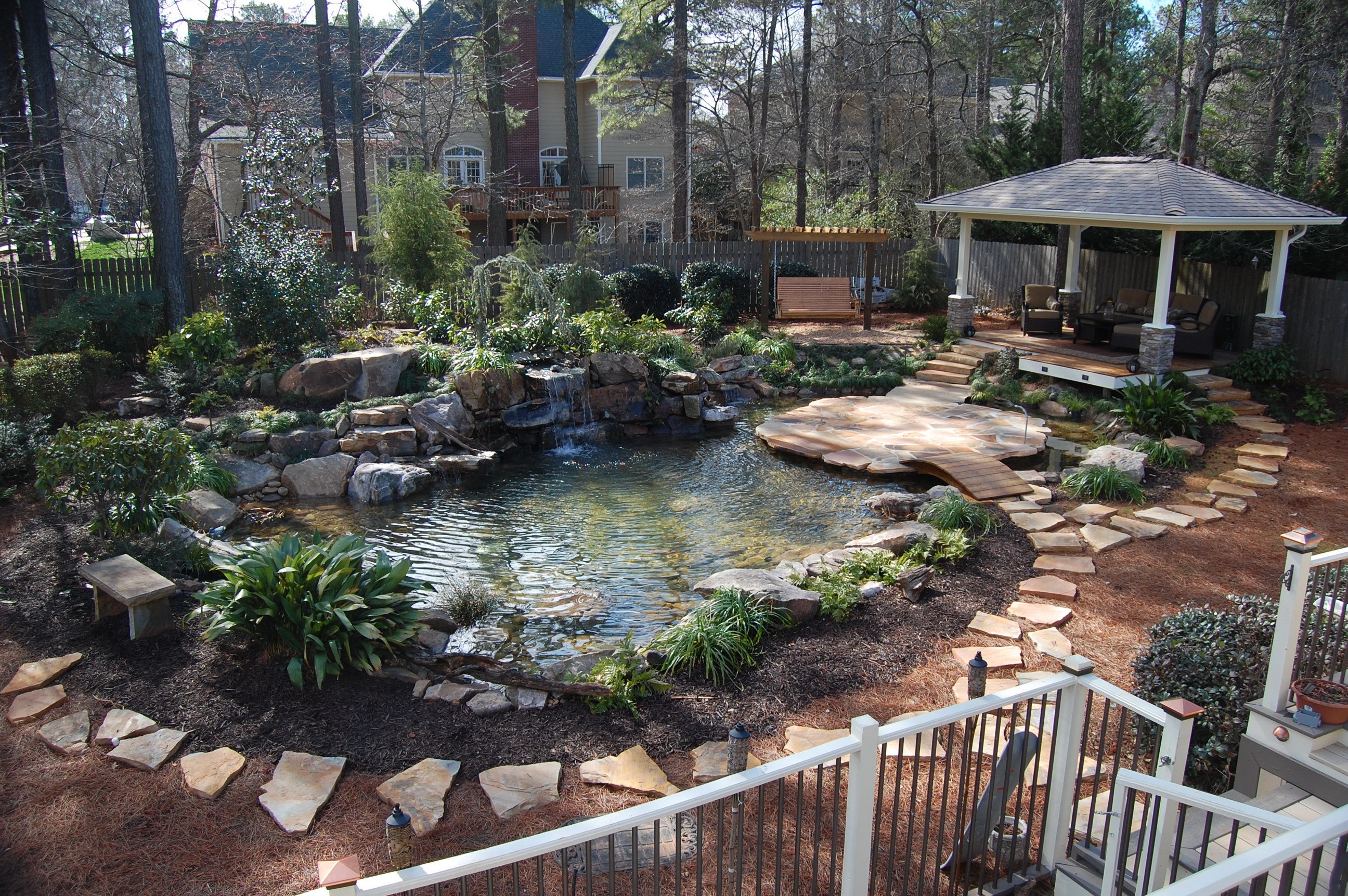 Backyard pond with waterfall, gazebo, and wooden swing HD Wallpaper