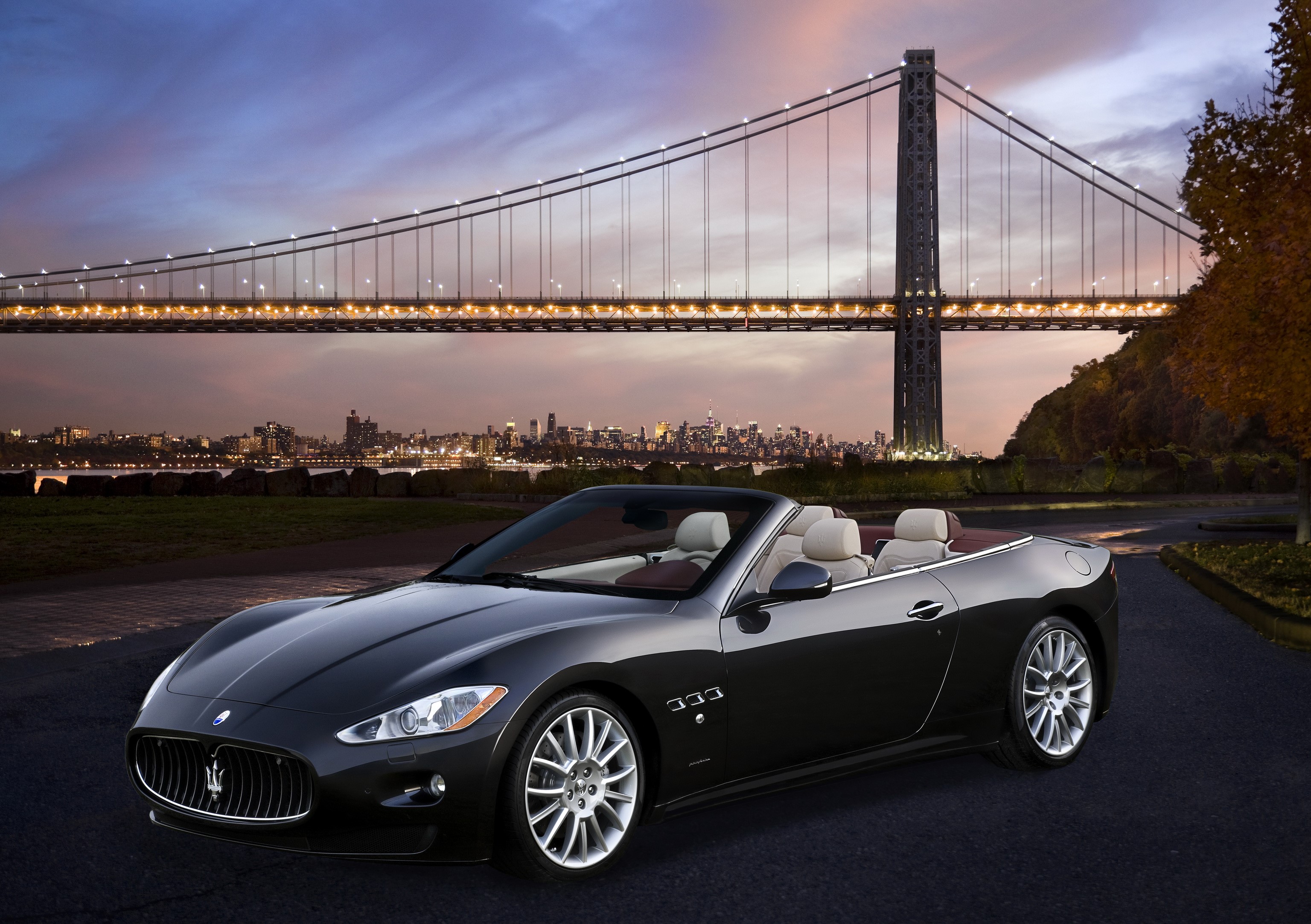 Black Maserati Gran Cabrio convertible by a bridge at dusk HD Wallpaper