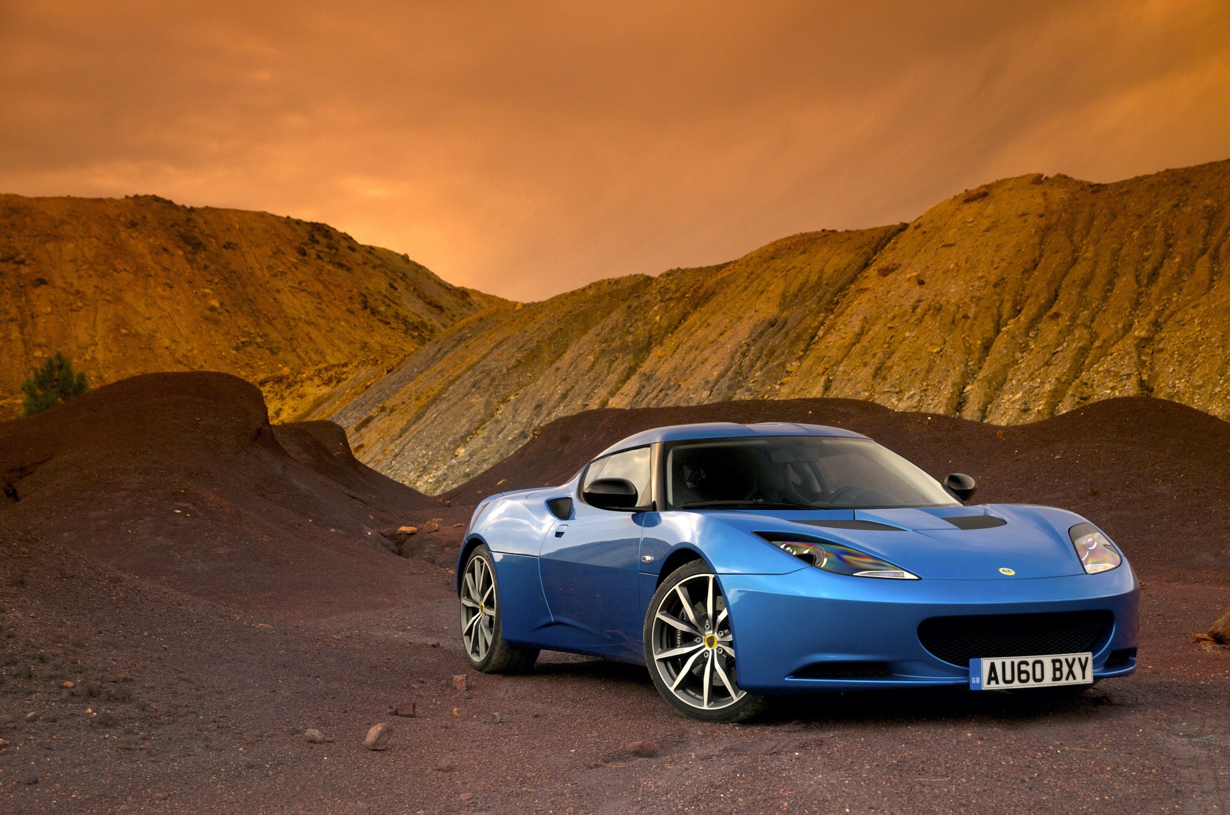 Blue Lotus Evora S parked in a rocky, barren landscape HD Wallpaper