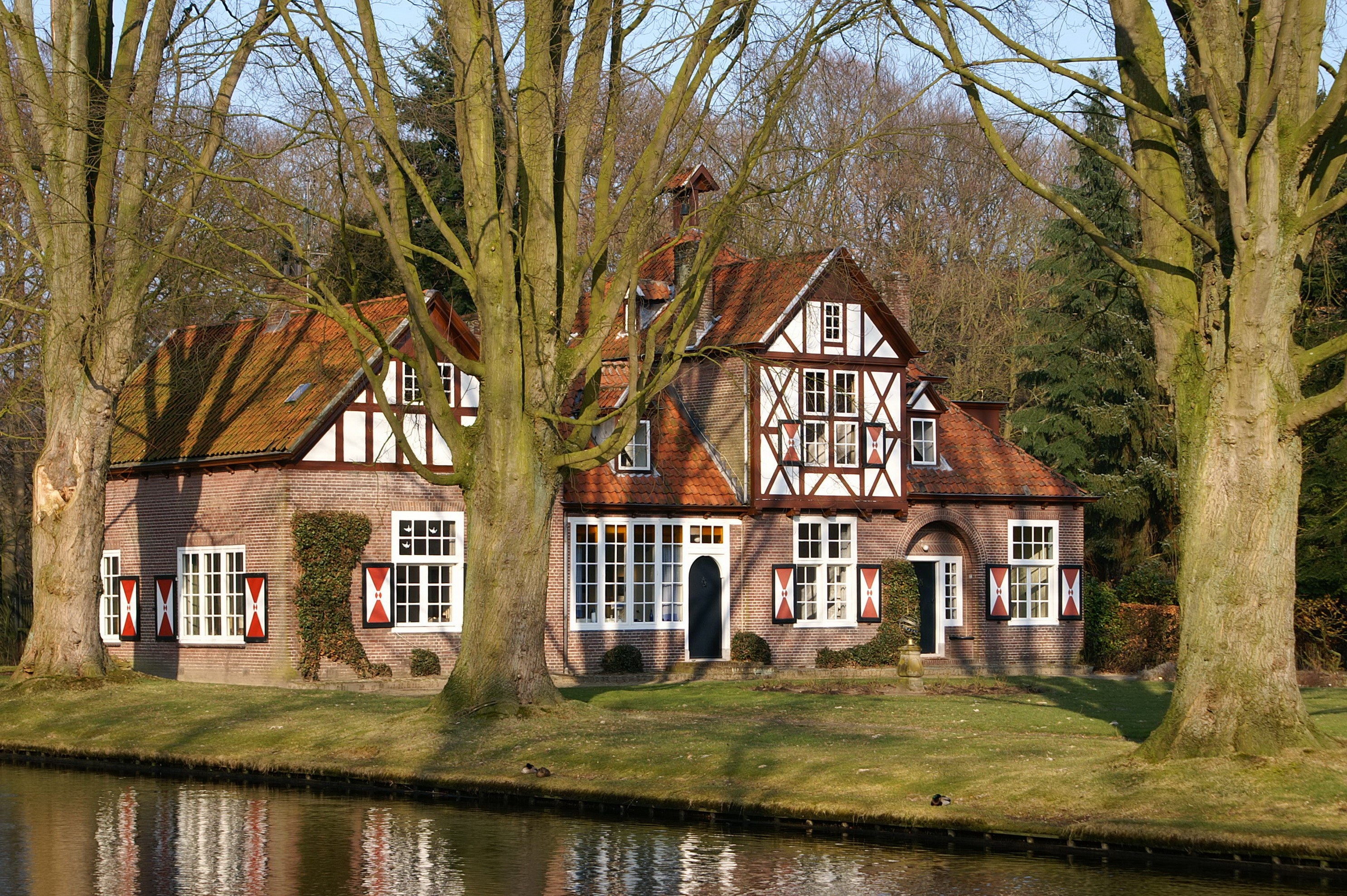 Tudor-style brick house with red shutters by a canal HD Wallpaper