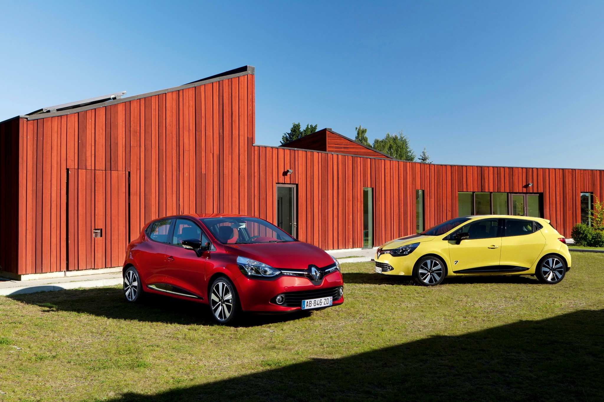 Red and yellow Renault Clio cars parked in front of a modern wooden building HD Wallpaper
