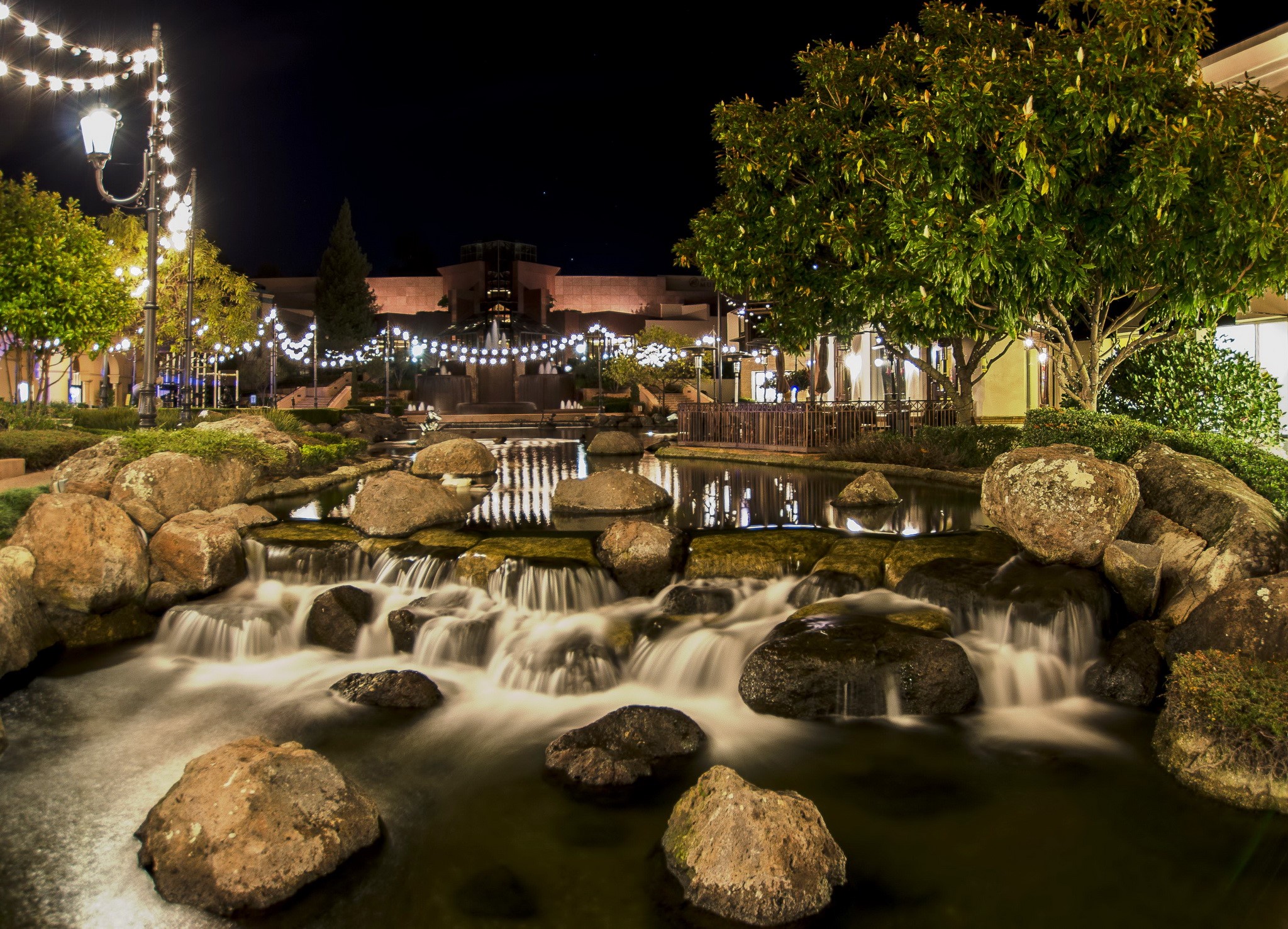 Night scene with illuminated string lights and a rock waterfall pond HD Wallpaper