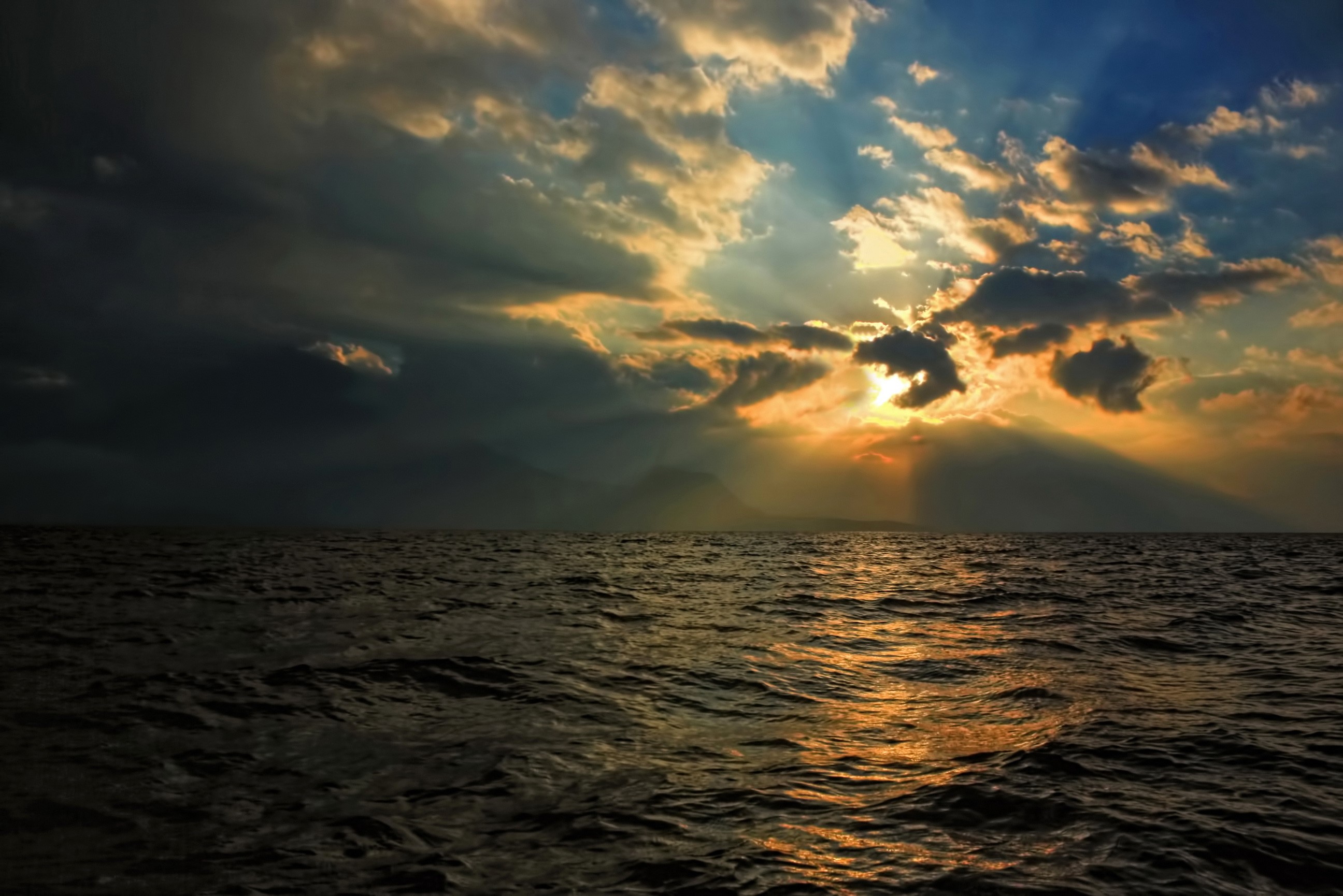 Sunset over a dark ocean with sun rays through clouds HD Wallpaper