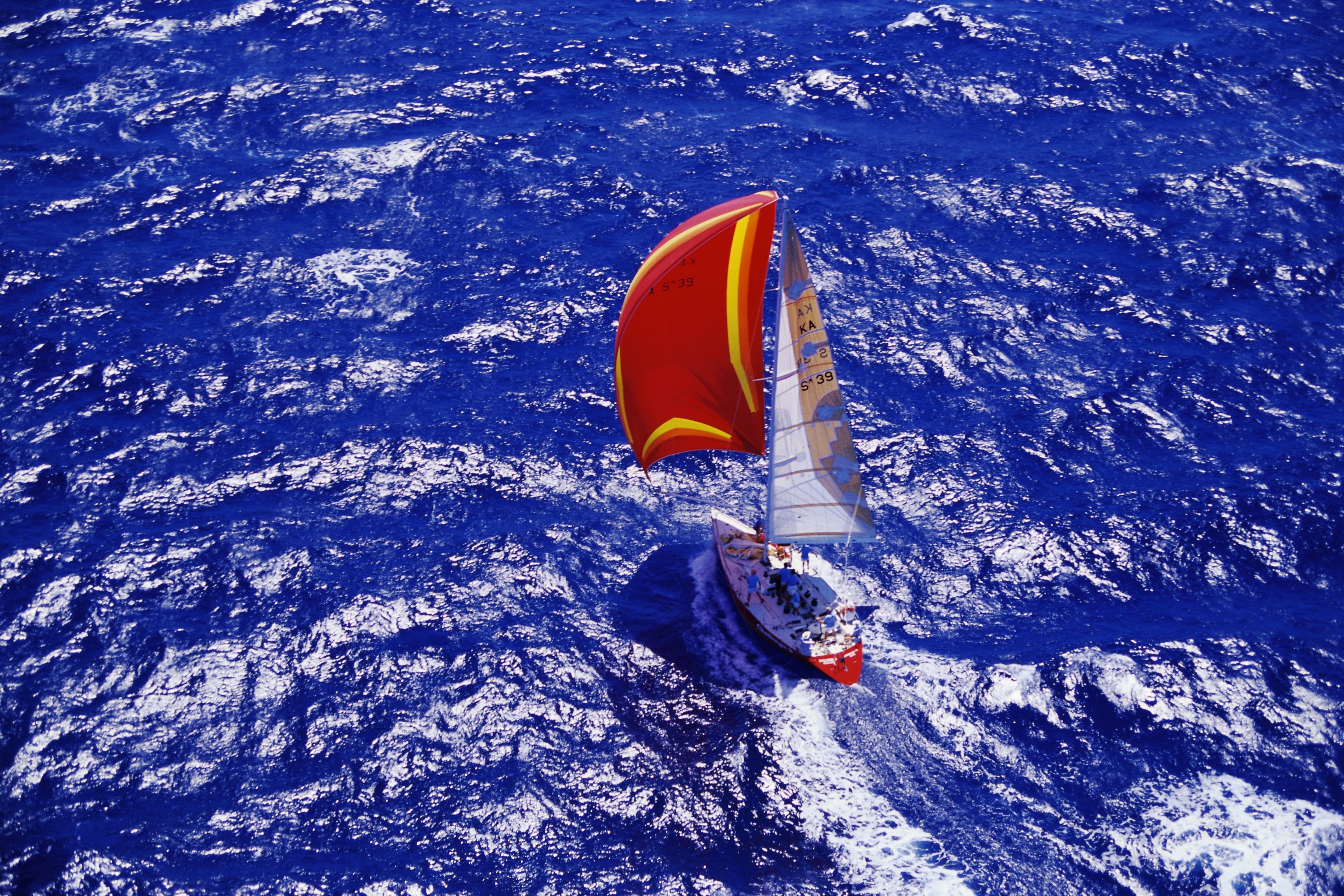 Sailboat with red and yellow sail on blue ocean HD Wallpaper
