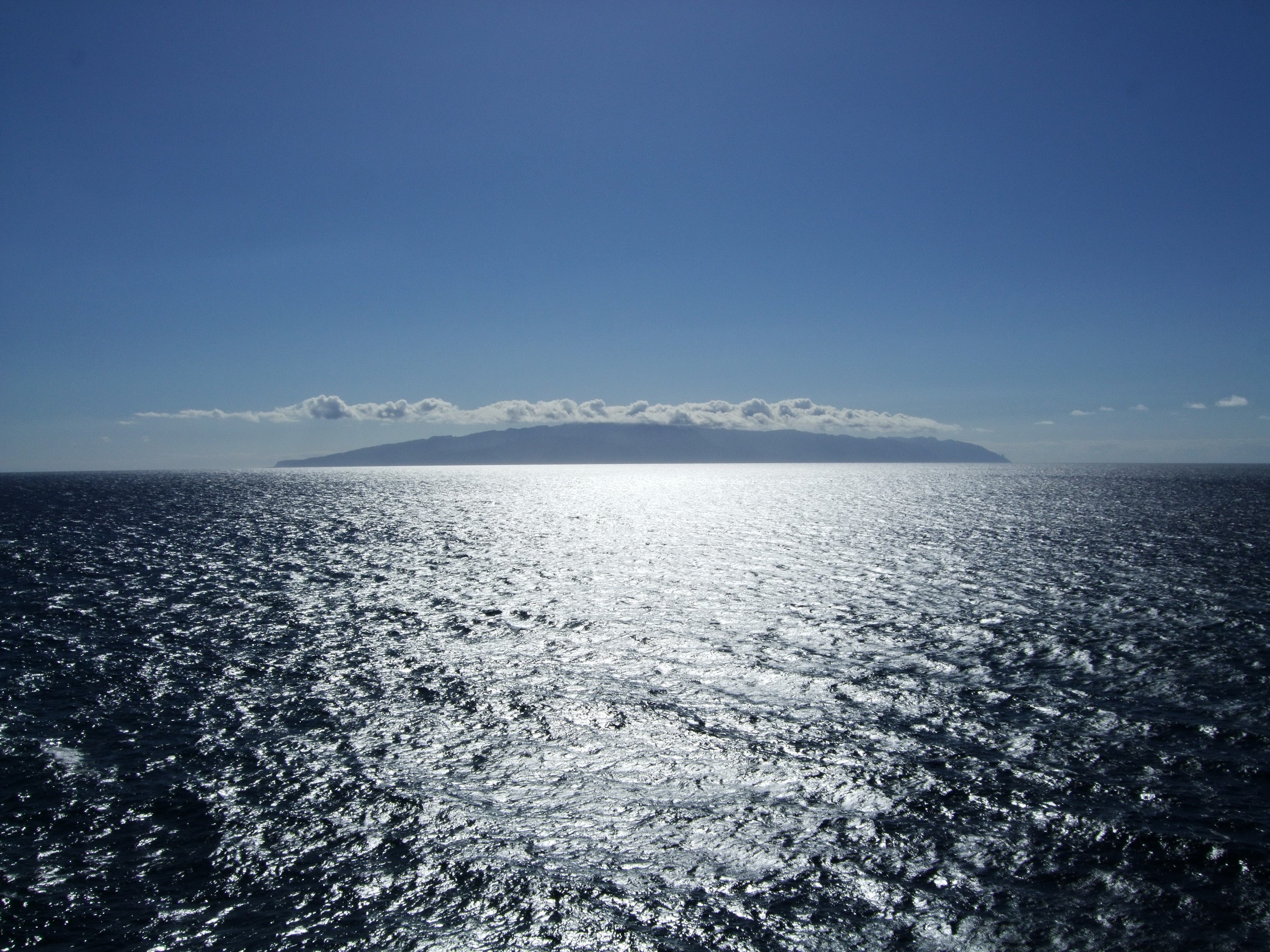 Island on the Horizon with Sunlit Ocean and Clouds HD Wallpaper