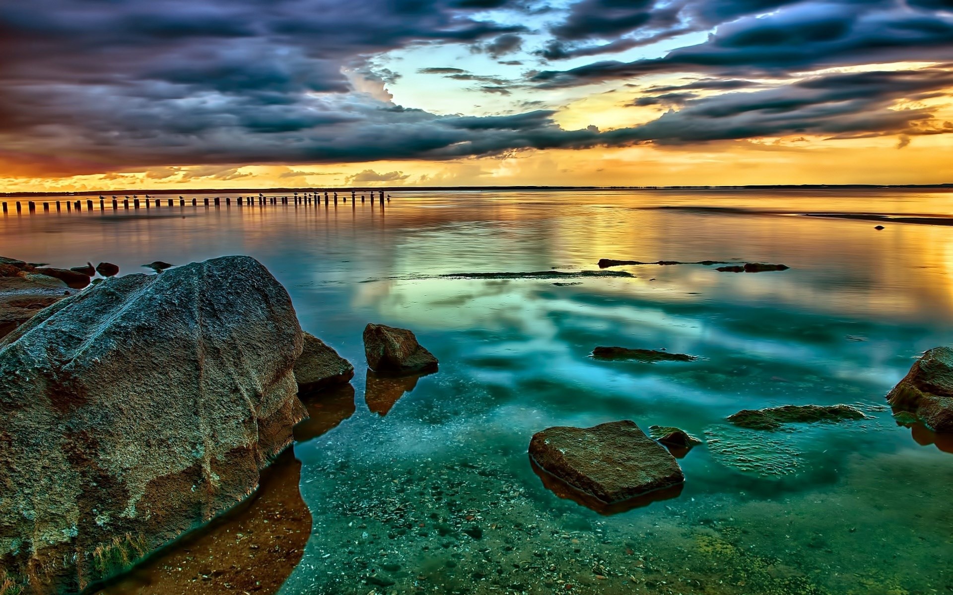 Rocky shore with calm water and dramatic sunset sky HD Wallpaper