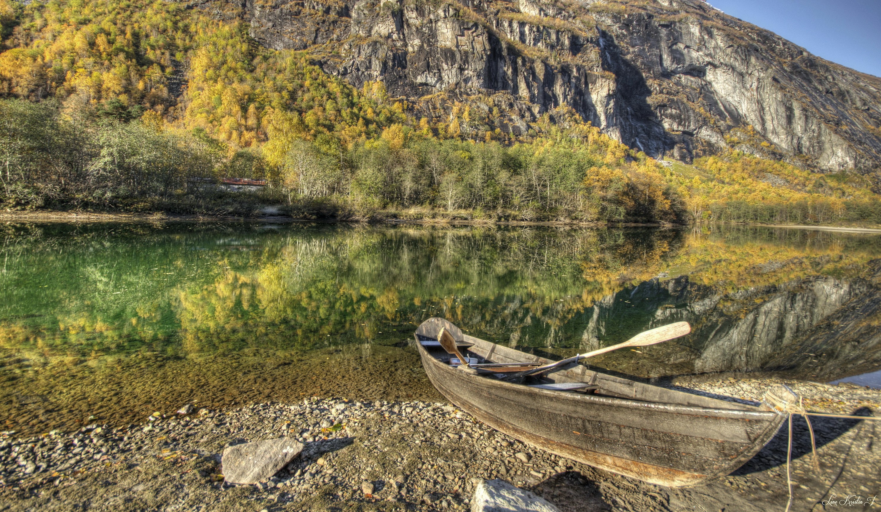 Wooden boat on a rocky shore with autumn trees and mountain reflection HD Wallpaper