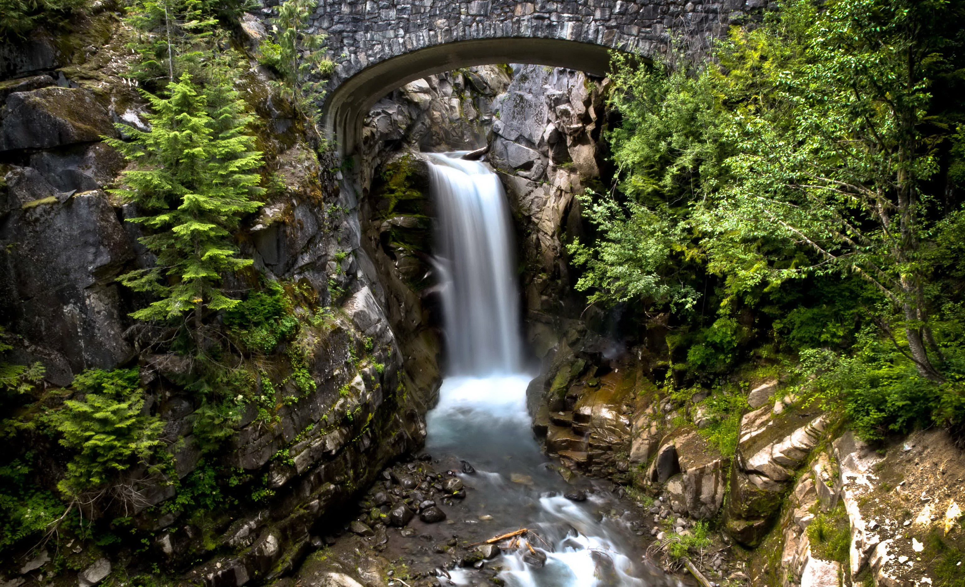 Waterfall under a stone bridge in Mount Rainier National Park HD Wallpaper