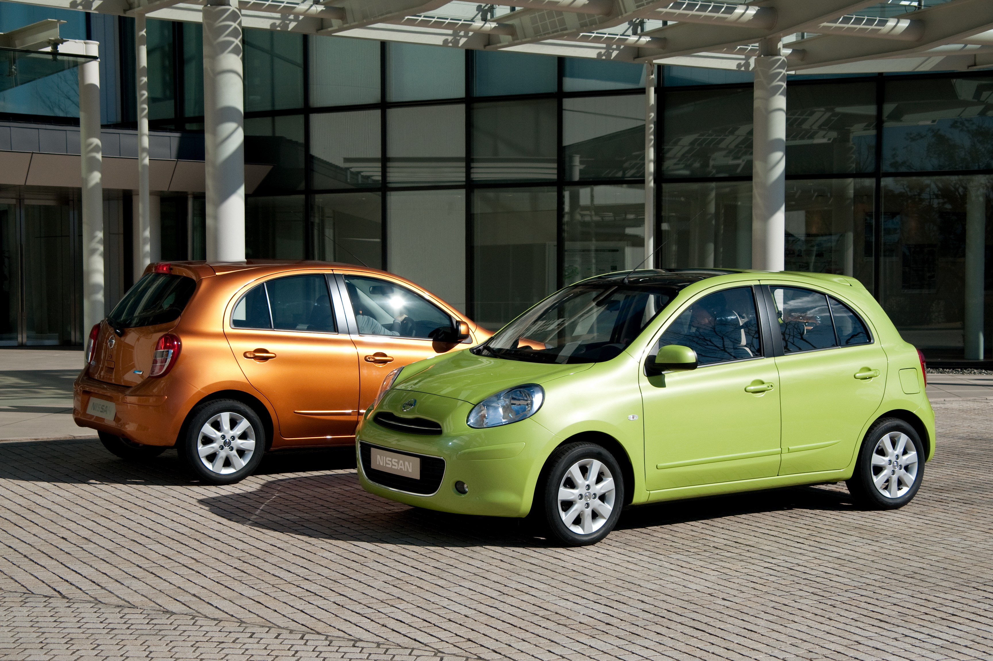 Two Nissan Micra cars parked outside a modern building HD Wallpaper