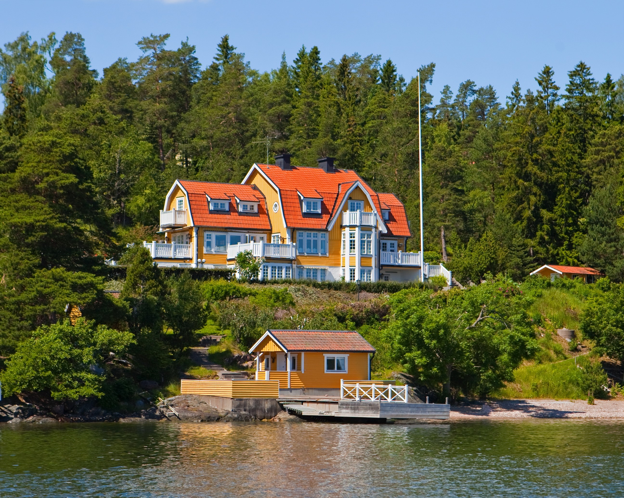 Yellow houses on a wooded hillside by the water in Resaro, Sweden HD Wallpaper