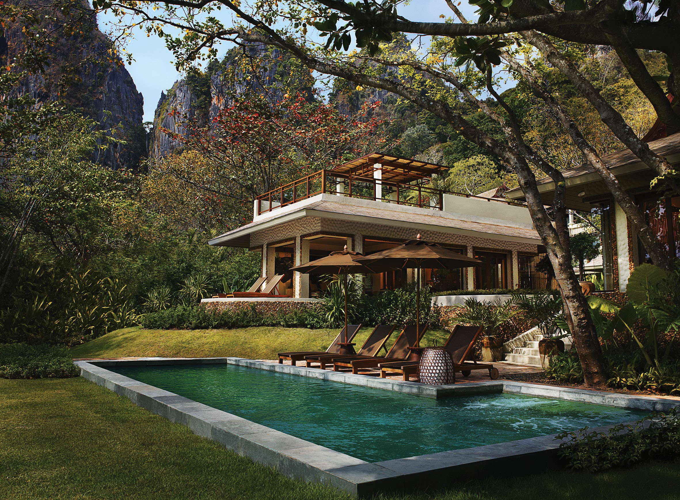 Resort pool with loungers and umbrellas near limestone cliffs in Thailand HD Wallpaper