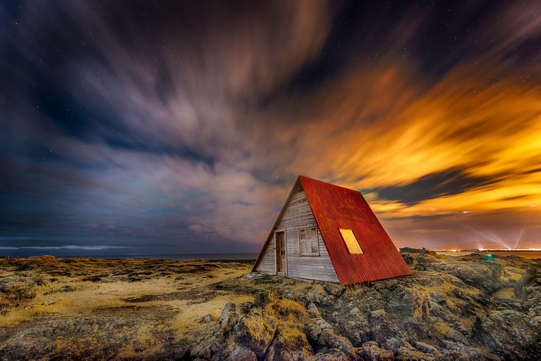 A-frame house on rocky terrain under a dramatic night sky in Iceland HD Wallpaper