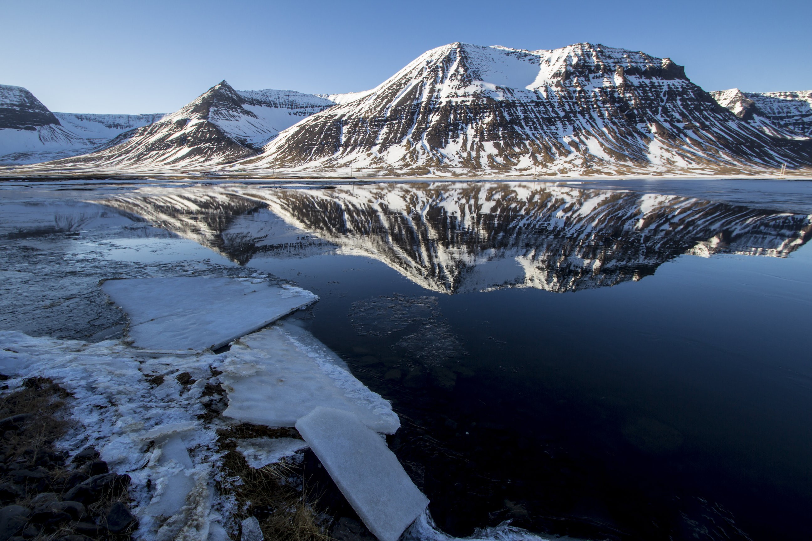 Snow-covered mountains reflected in a calm lake with ice HD Wallpaper