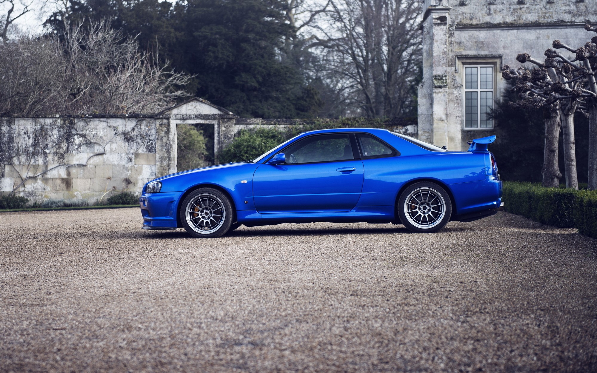 Blue Nissan Skyline R34 GT-R parked in front of a stone building HD Wallpaper
