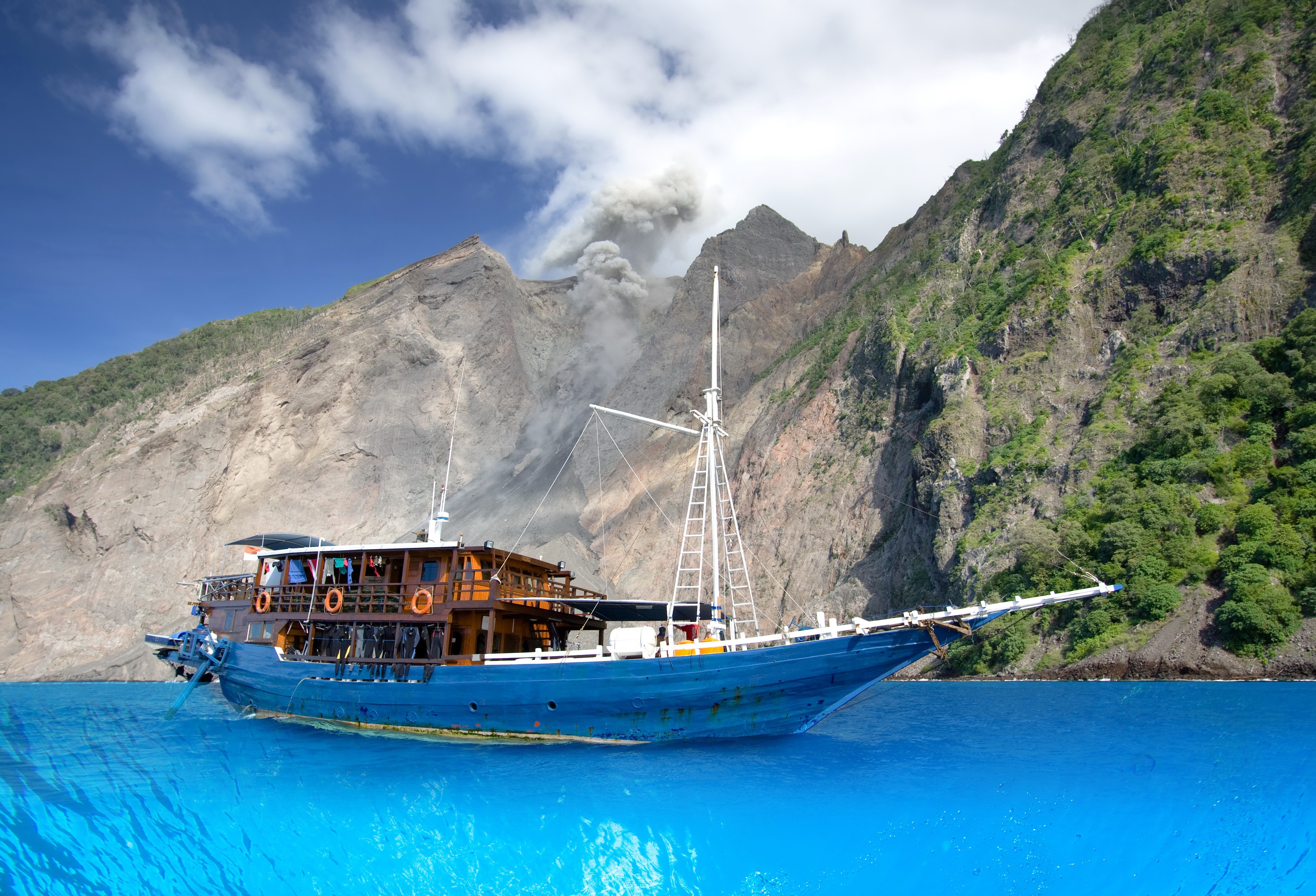 Blue boat near volcanic mountains with smoke HD Wallpaper