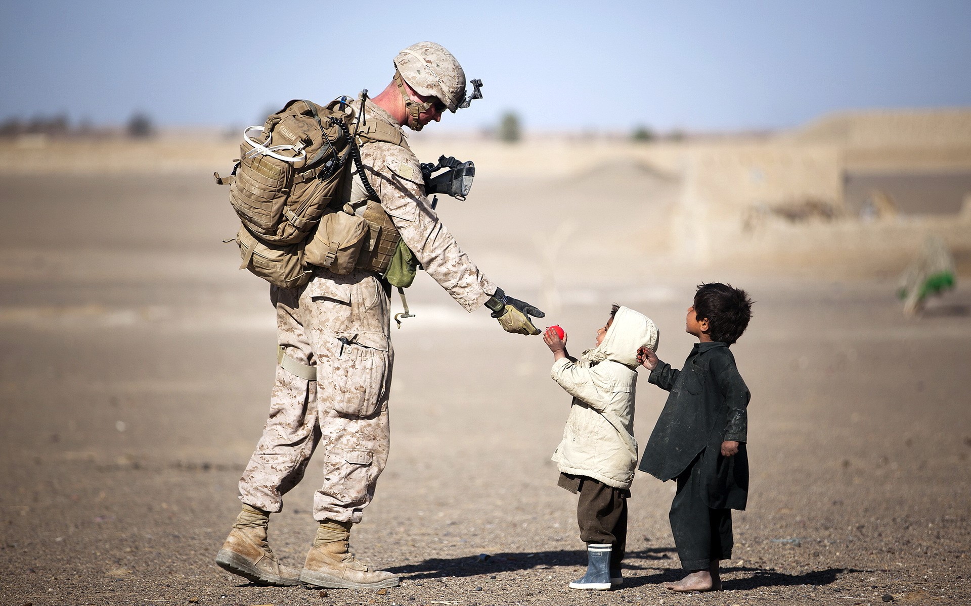 Soldier gives toy to children in desert HD Wallpaper