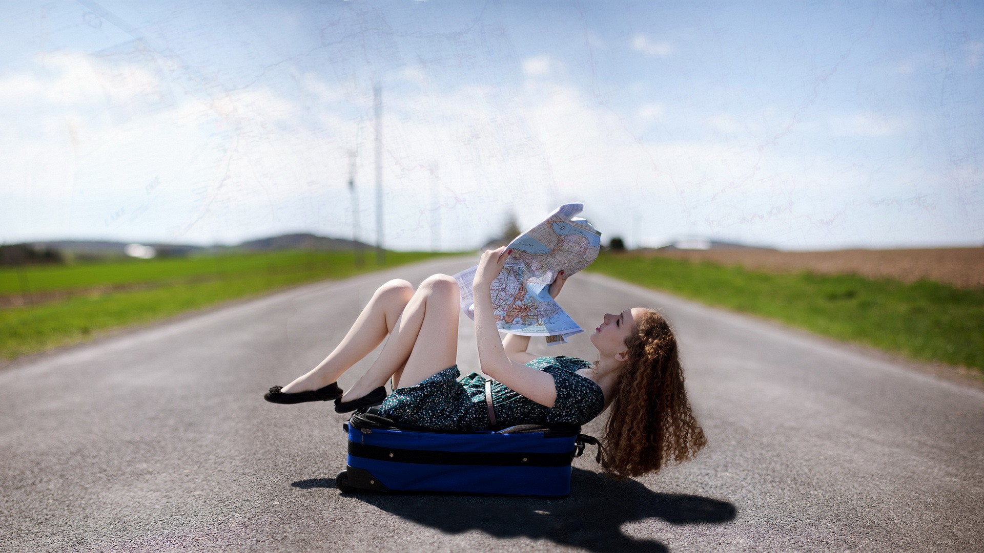 Woman lying on a suitcase on a road with a map HD Wallpaper