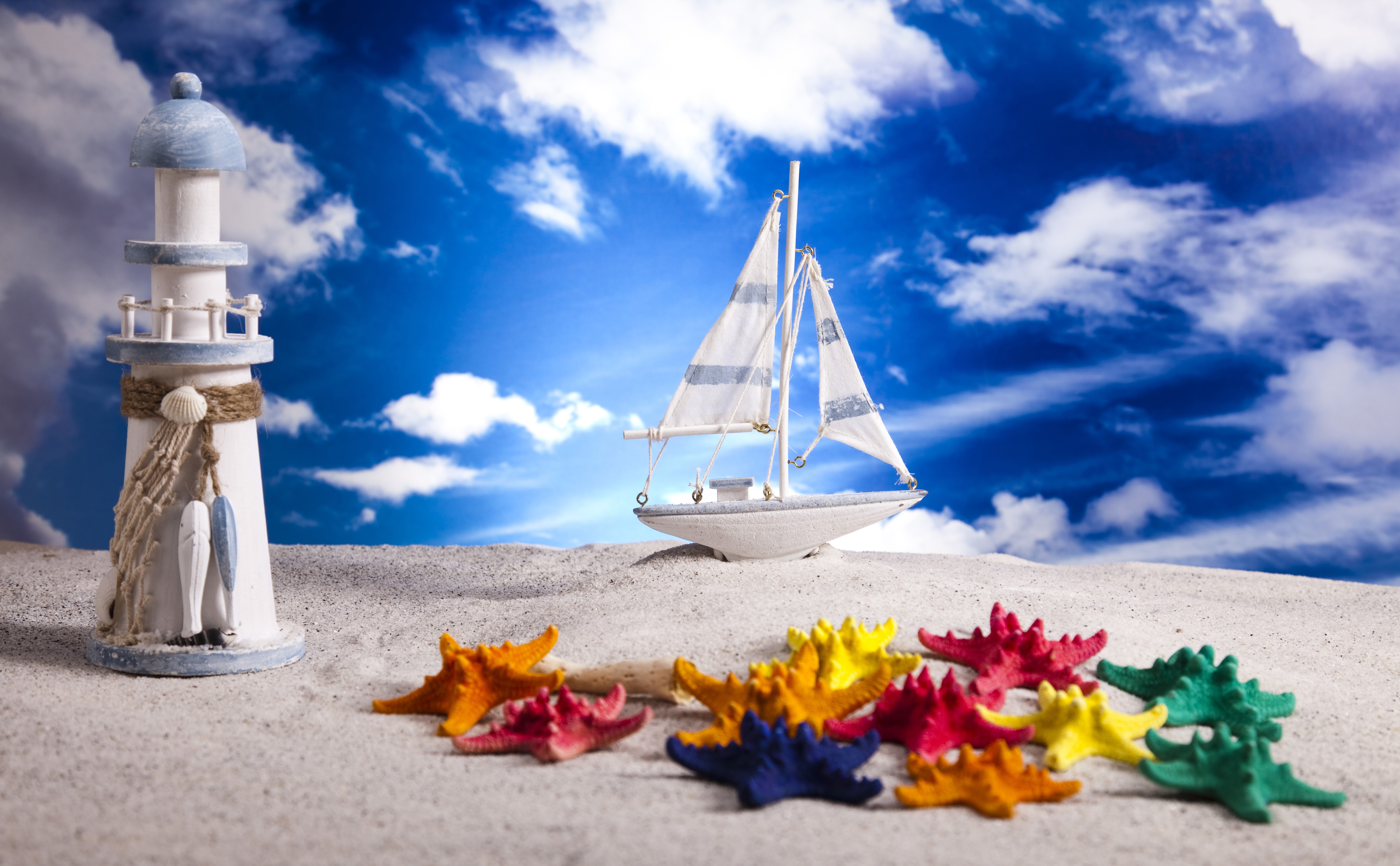 Toy lighthouse, sailboat, and starfish on sand with sky background HD Wallpaper