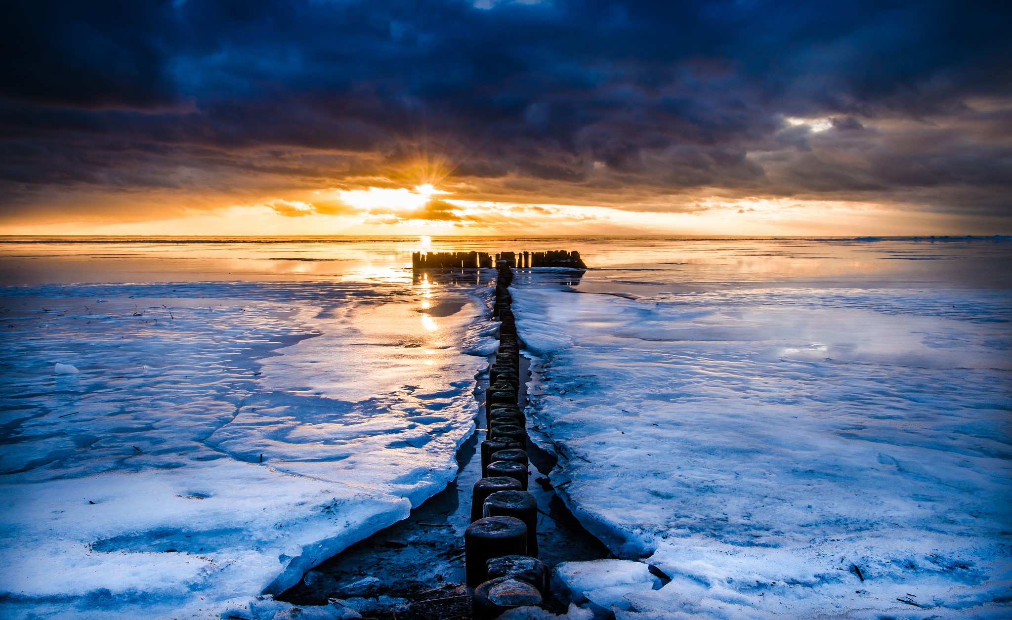 Sunset over icy sea with wooden breakwater HD Wallpaper