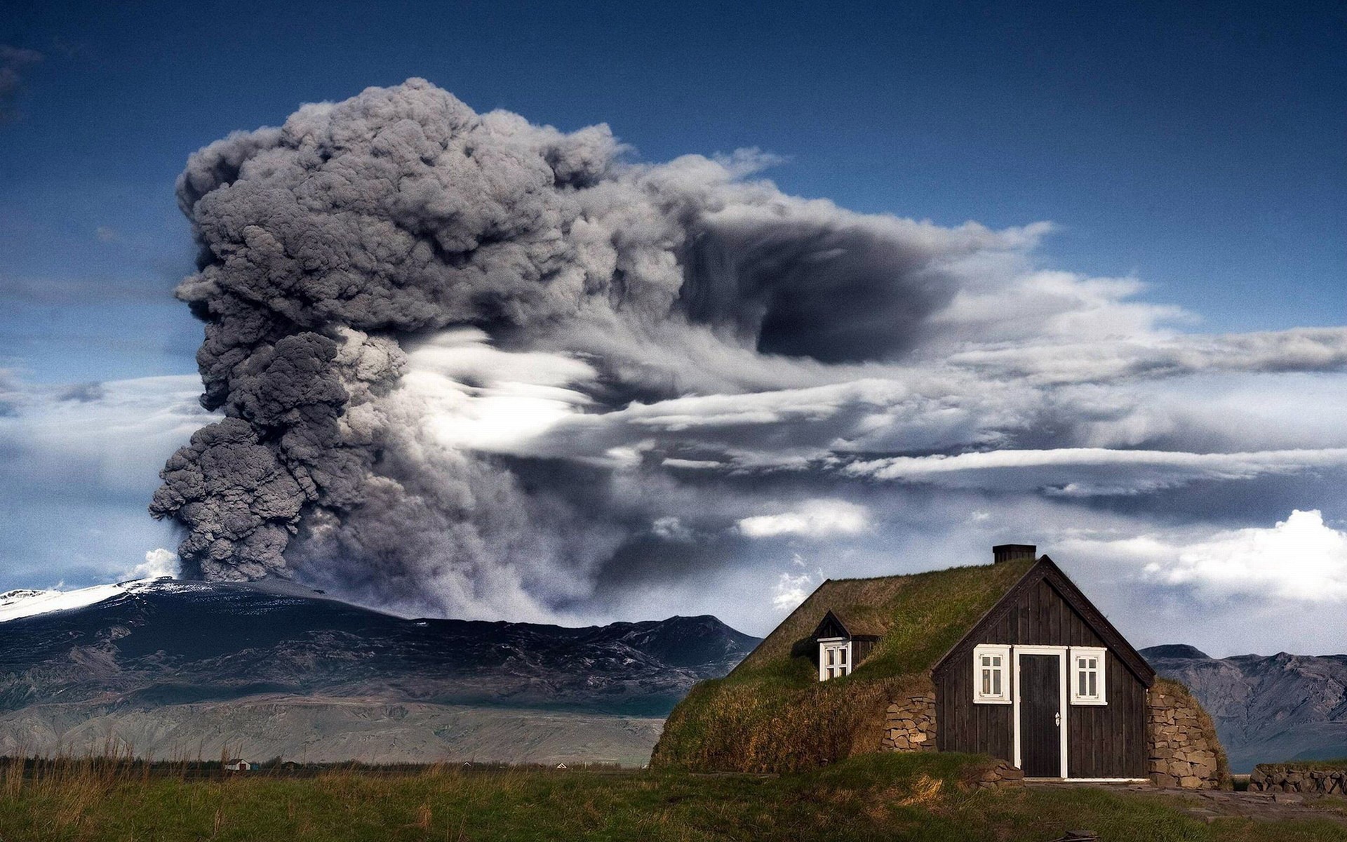 Volcanic eruption with smoke plume over mountains and a house HD Wallpaper