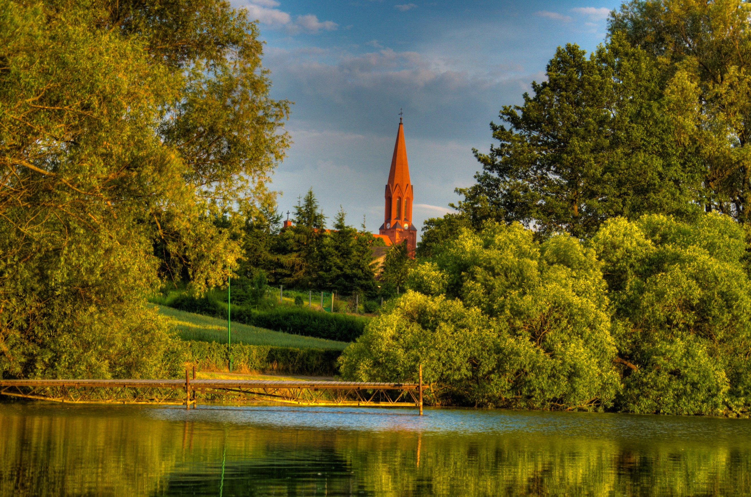 Church tower over trees by a lake in Gmina Cekcyn, Poland HD Wallpaper