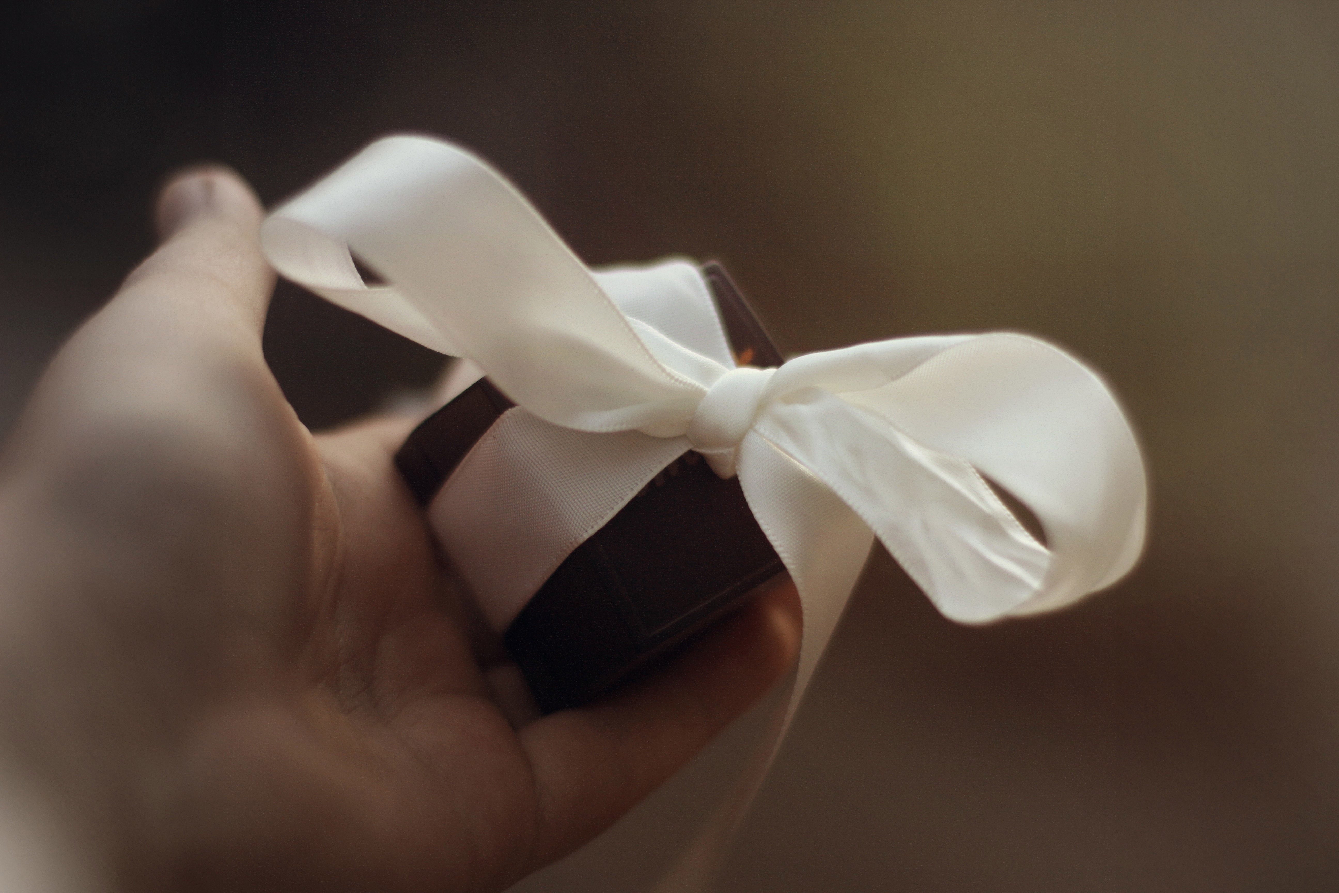 Hand holding a gift with a white ribbon HD Wallpaper