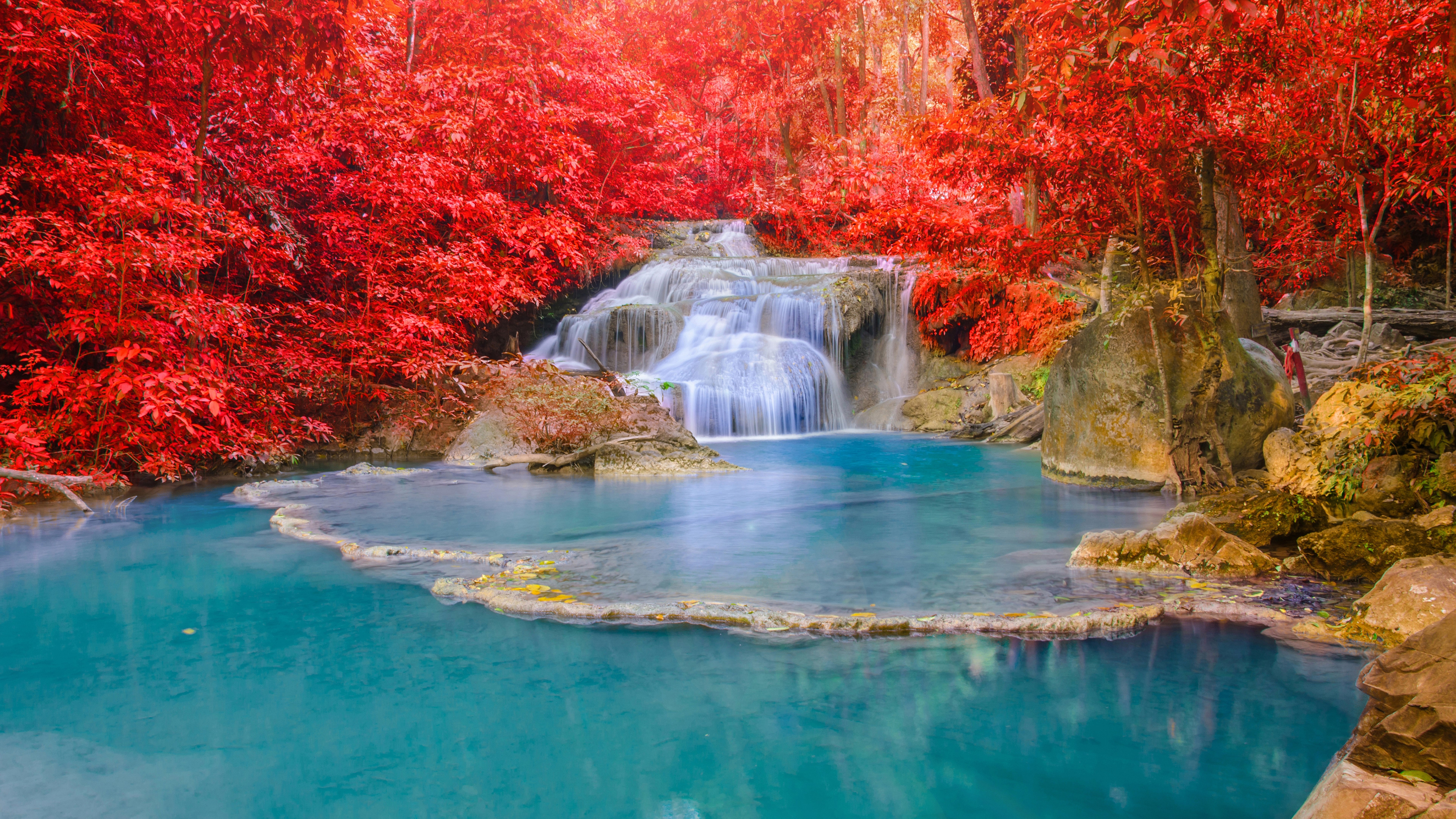 Waterfall cascading into a turquoise pool surrounded by red foliage HD Wallpaper