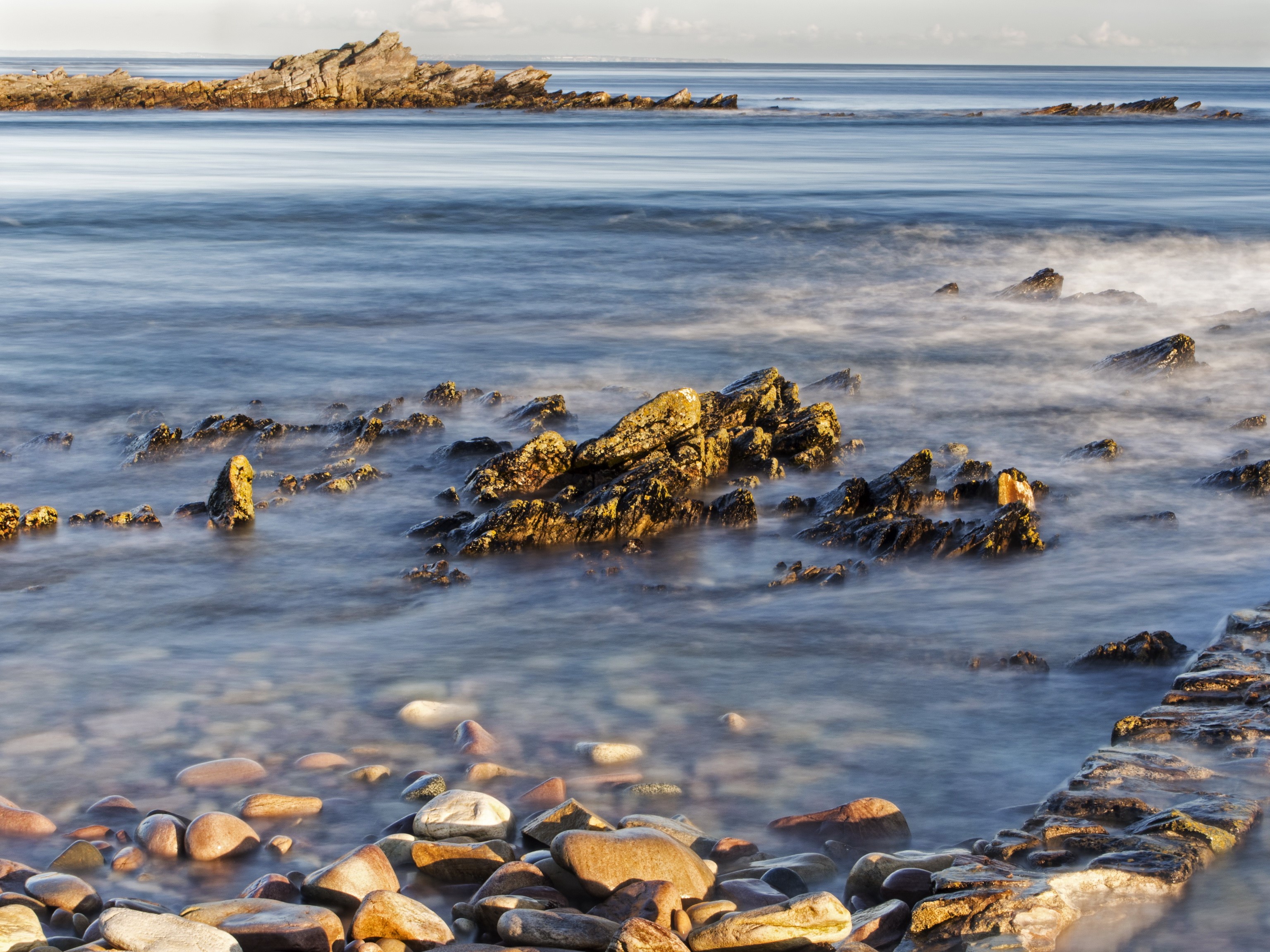 Rocky coastline with smooth stones and the sea HD Wallpaper