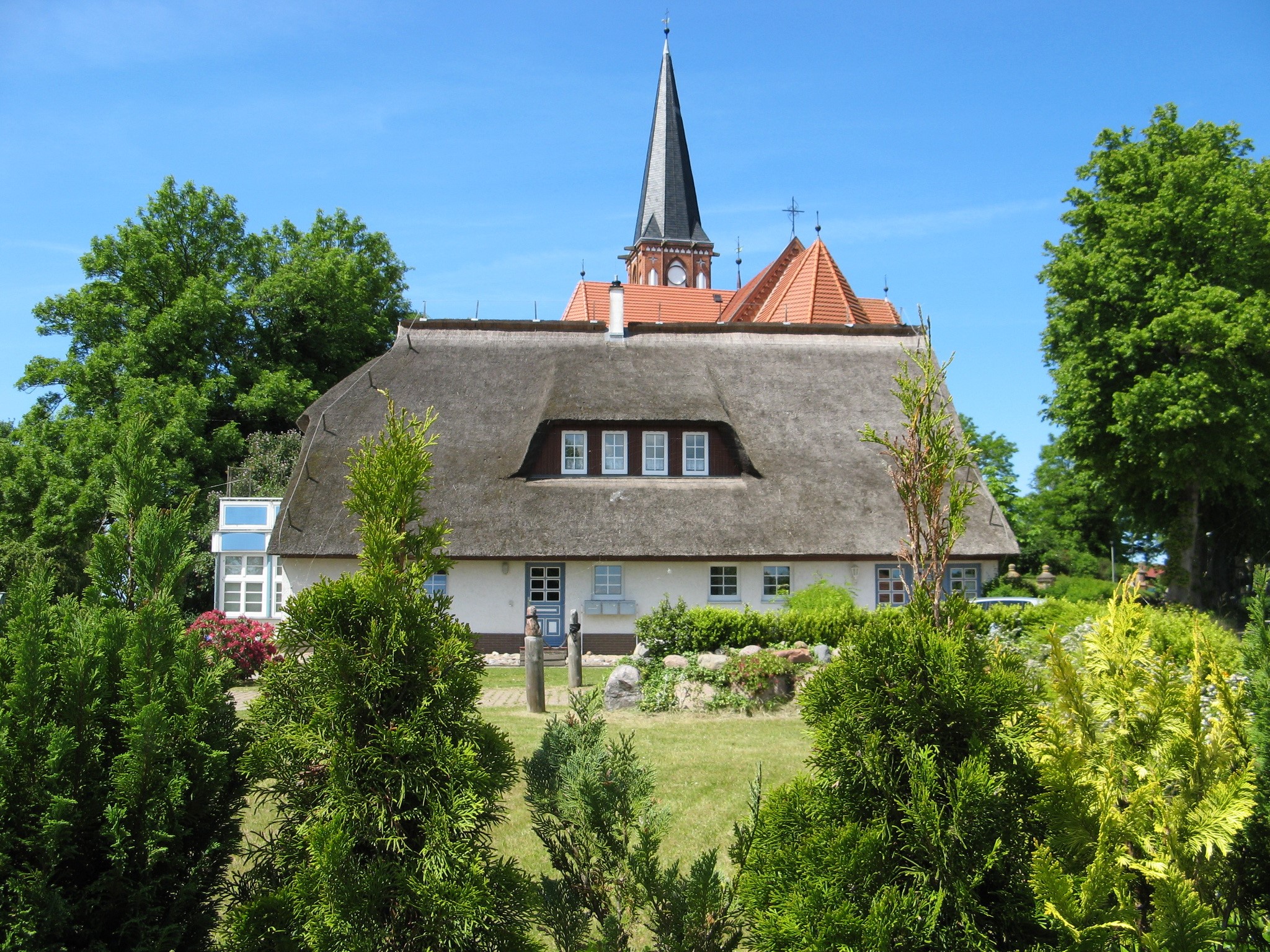 Thatched roof house with church spire in Wustrow, Germany HD Wallpaper