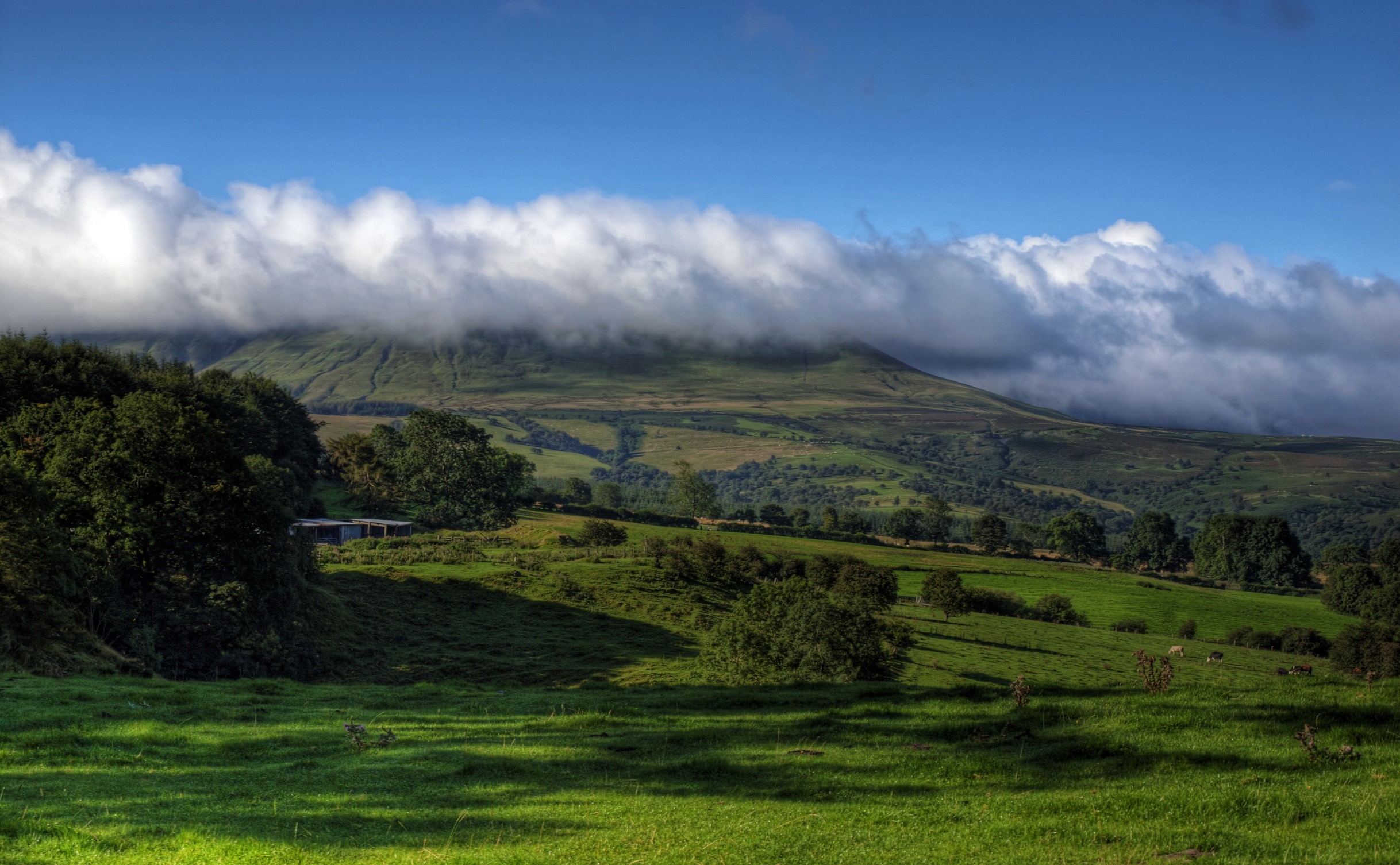 Rolling green hills with clouds over mountains in Wales HD Wallpaper