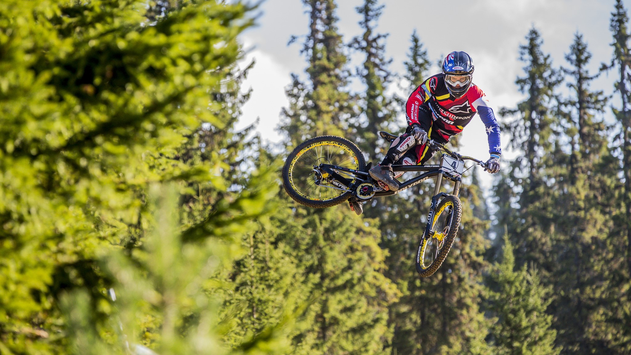 Mountain biker in mid-air jump over trees HD Wallpaper