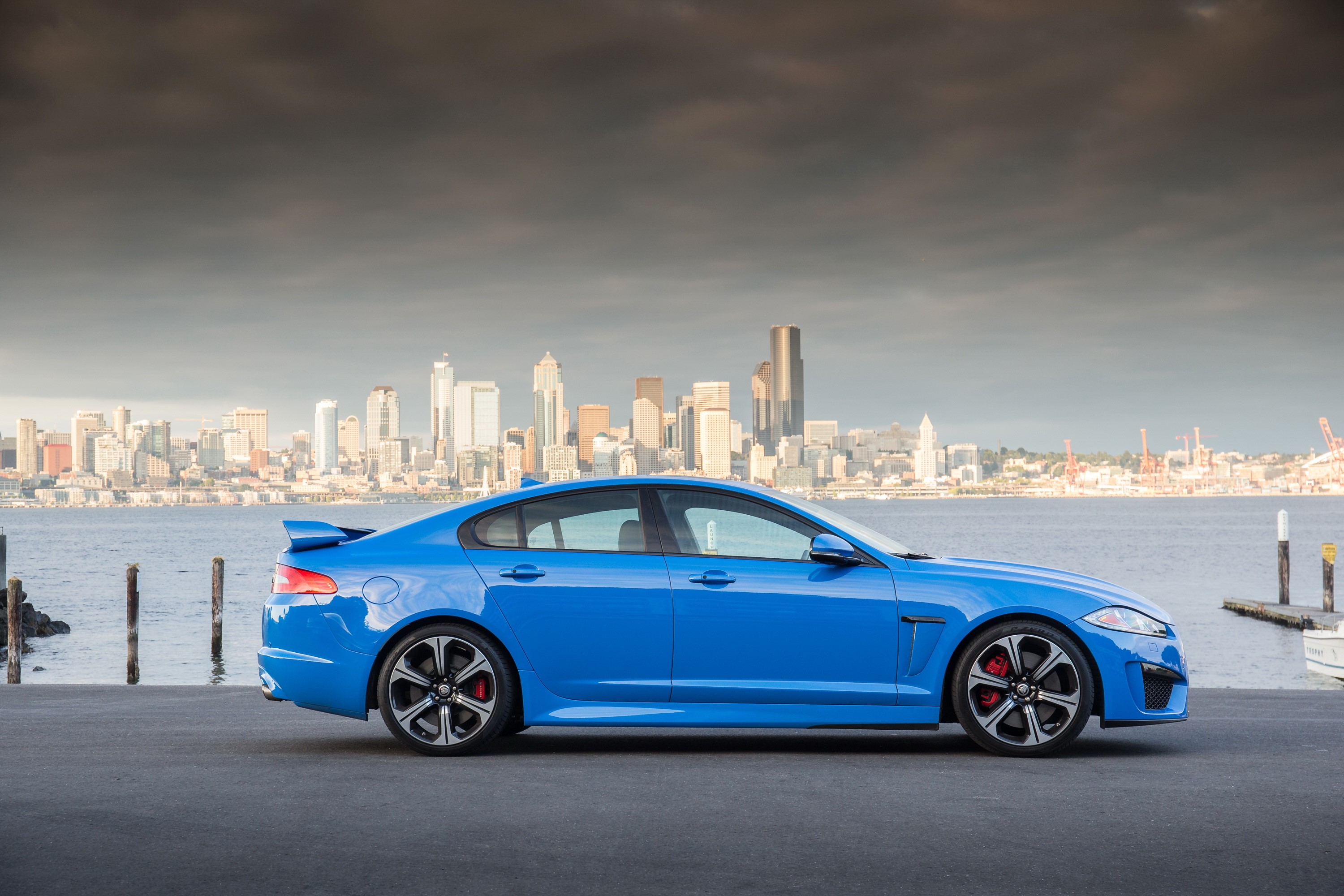 Blue Jaguar XFR-S parked by a city skyline HD Wallpaper