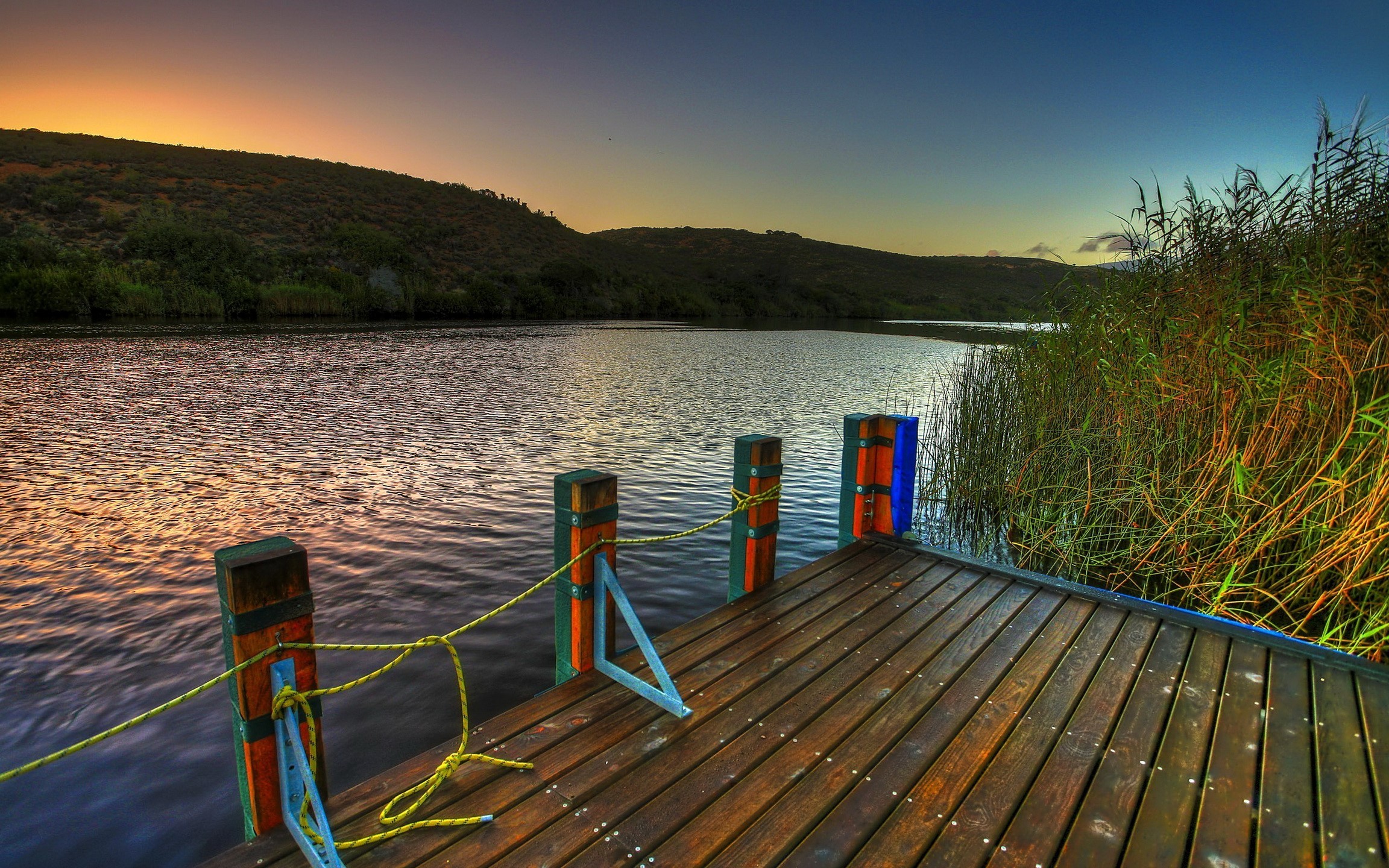 Wooden dock on a river at sunset with reeds HD Wallpaper