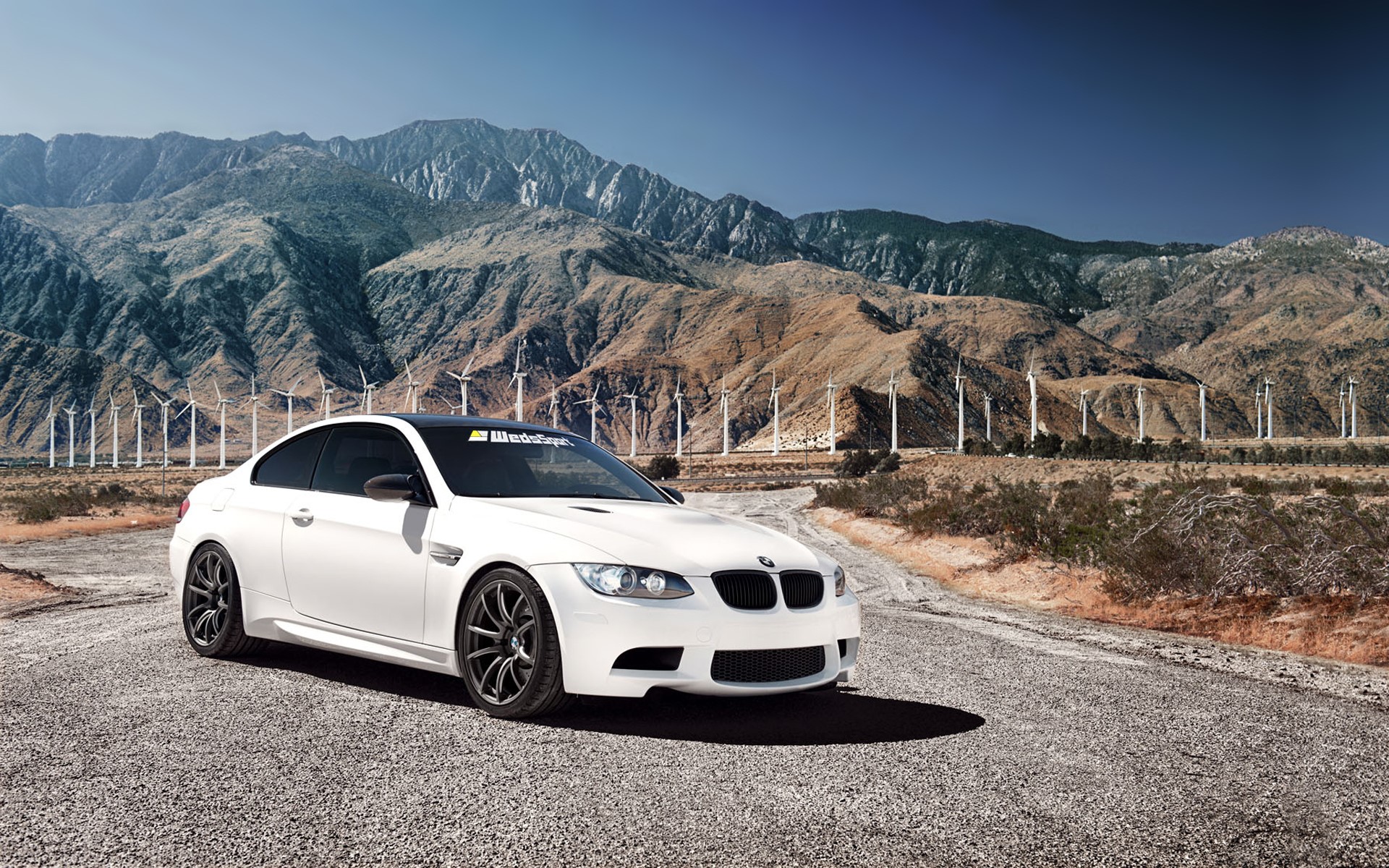 White BMW M3 parked on a road with windmills and mountains HD Wallpaper