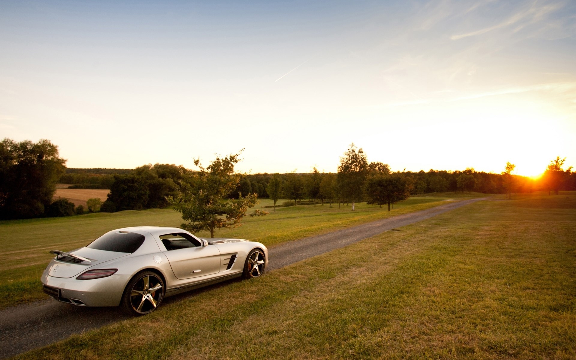 Silver Mercedes-Benz SLS on a dirt road at sunset HD Wallpaper