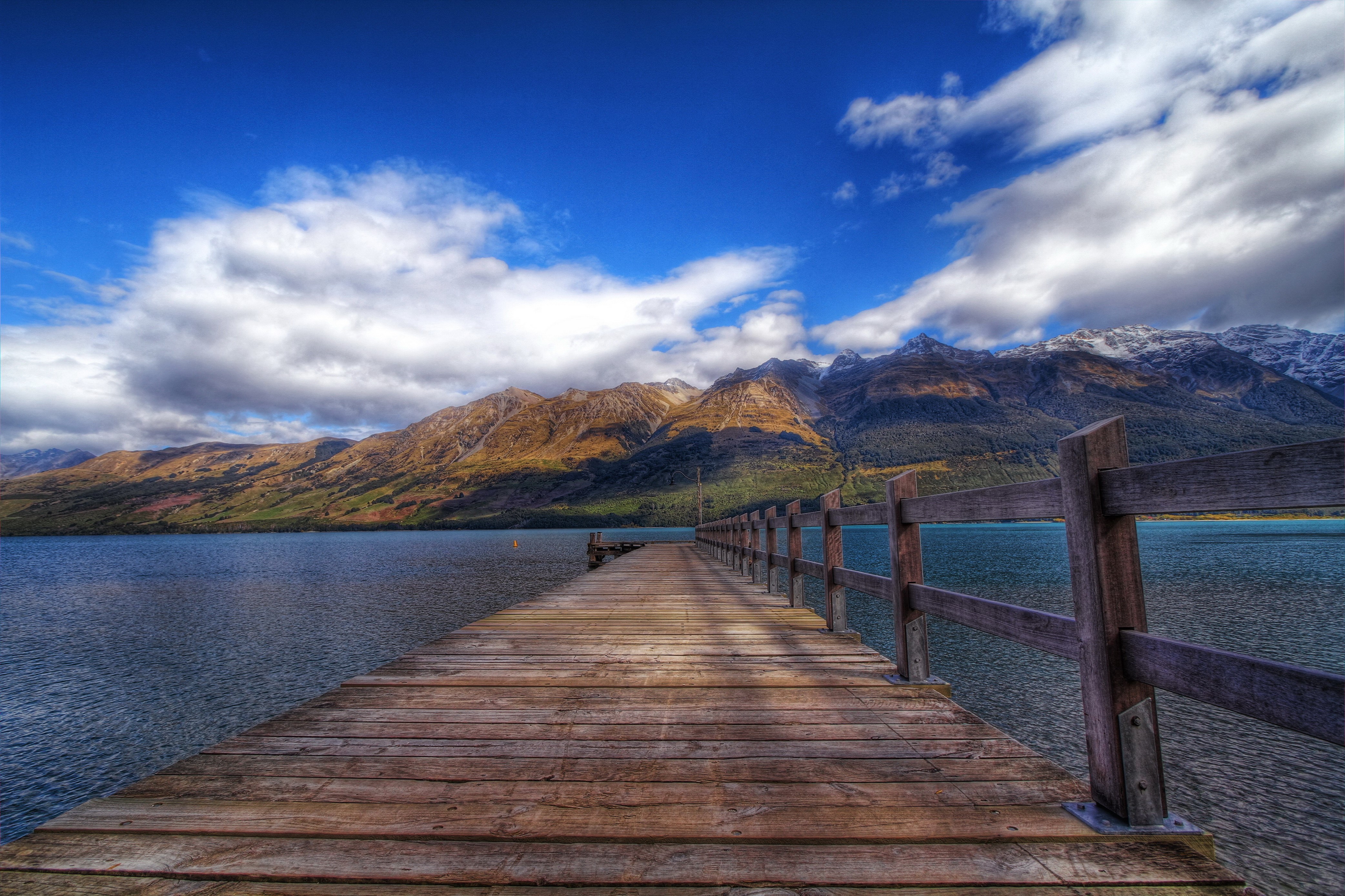 Wooden pier on a lake with mountains and clouds HD Wallpaper