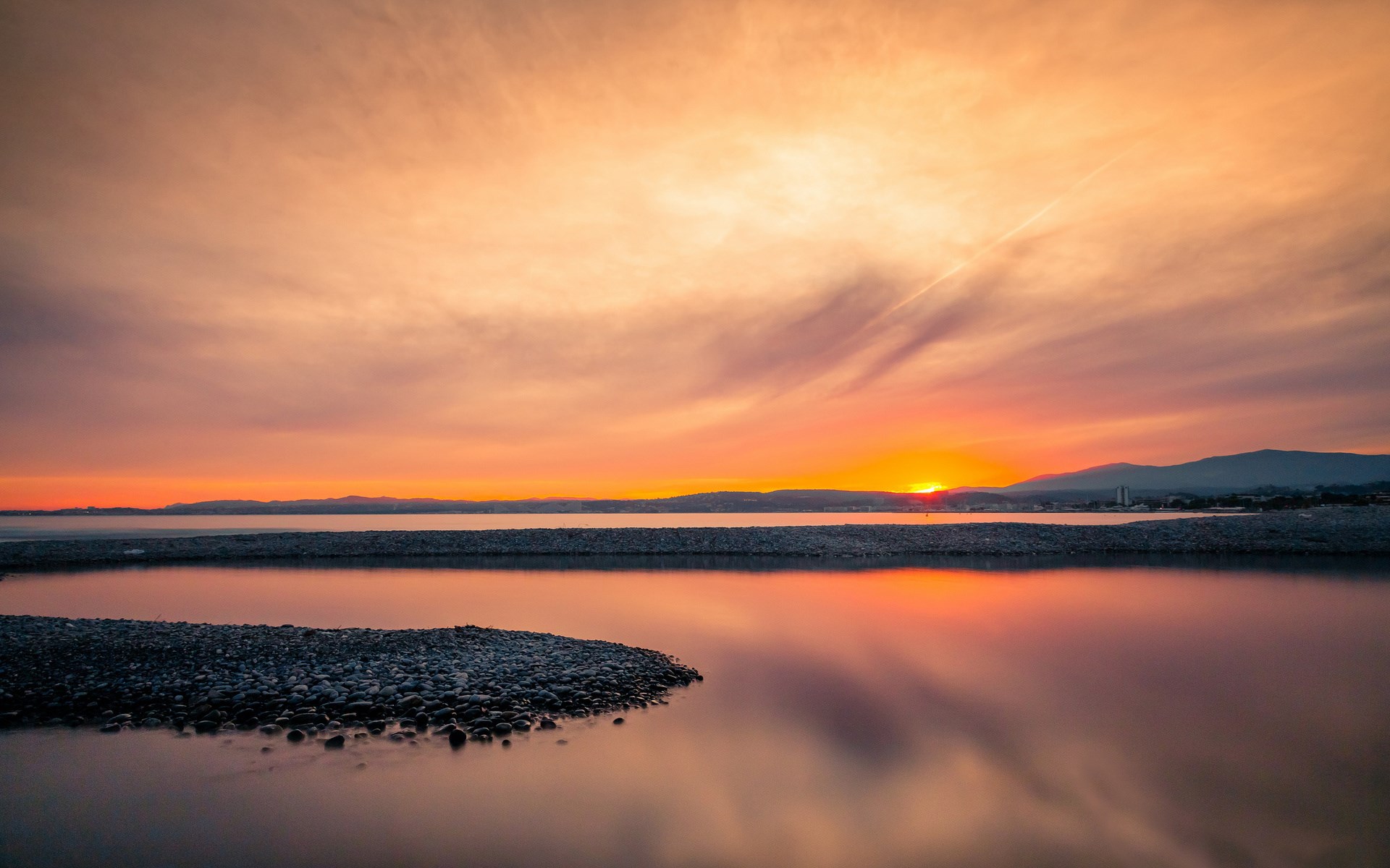Sunset over a calm body of water with mountains in the distance HD Wallpaper