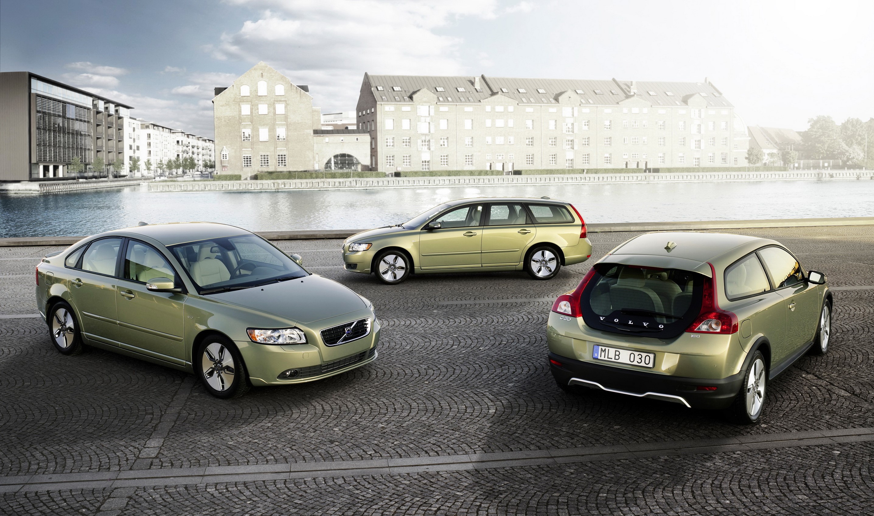 Three Volvo cars parked on cobblestone by a canal HD Wallpaper