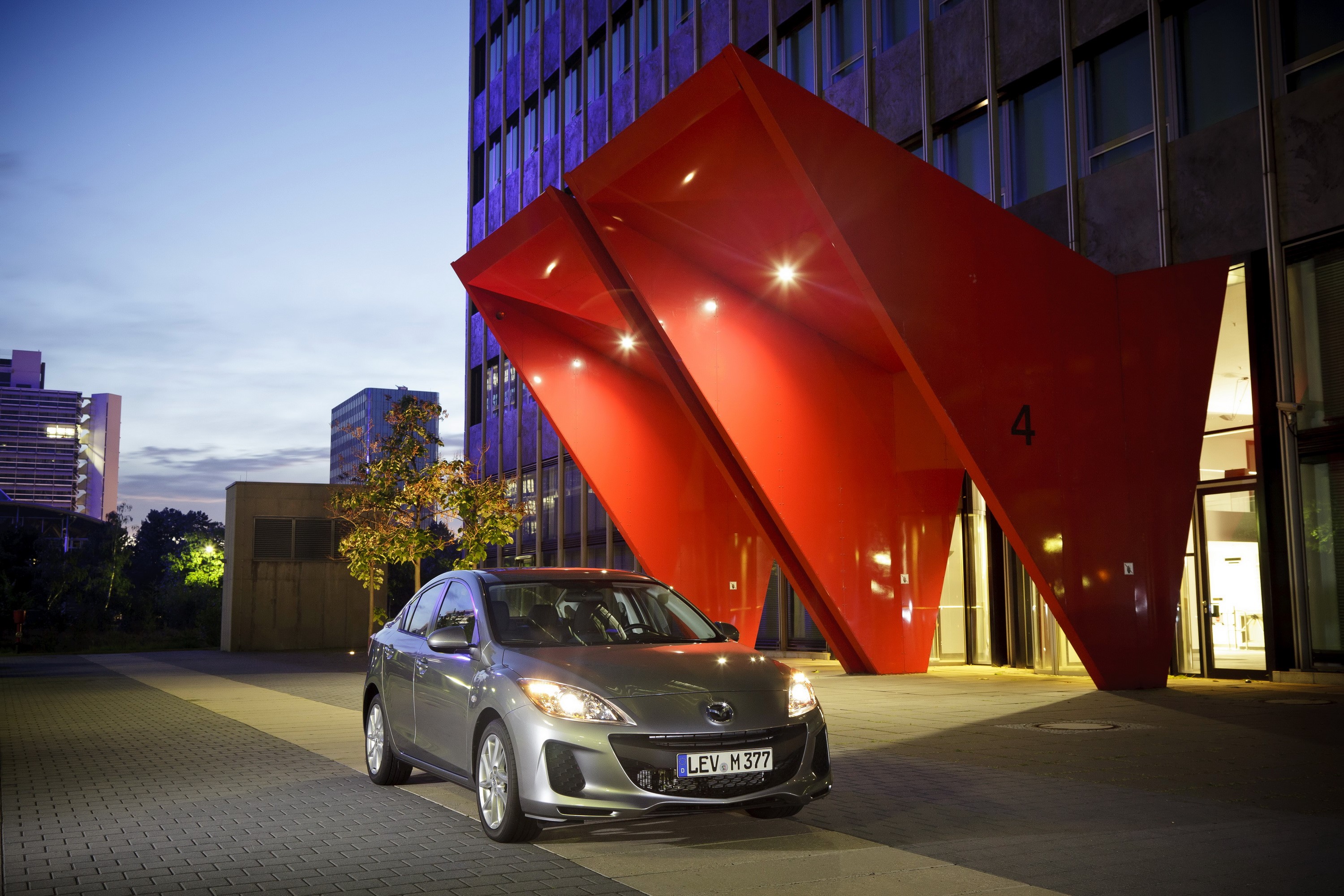 2011 Mazda 3 sedan parked outside modern building HD Wallpaper