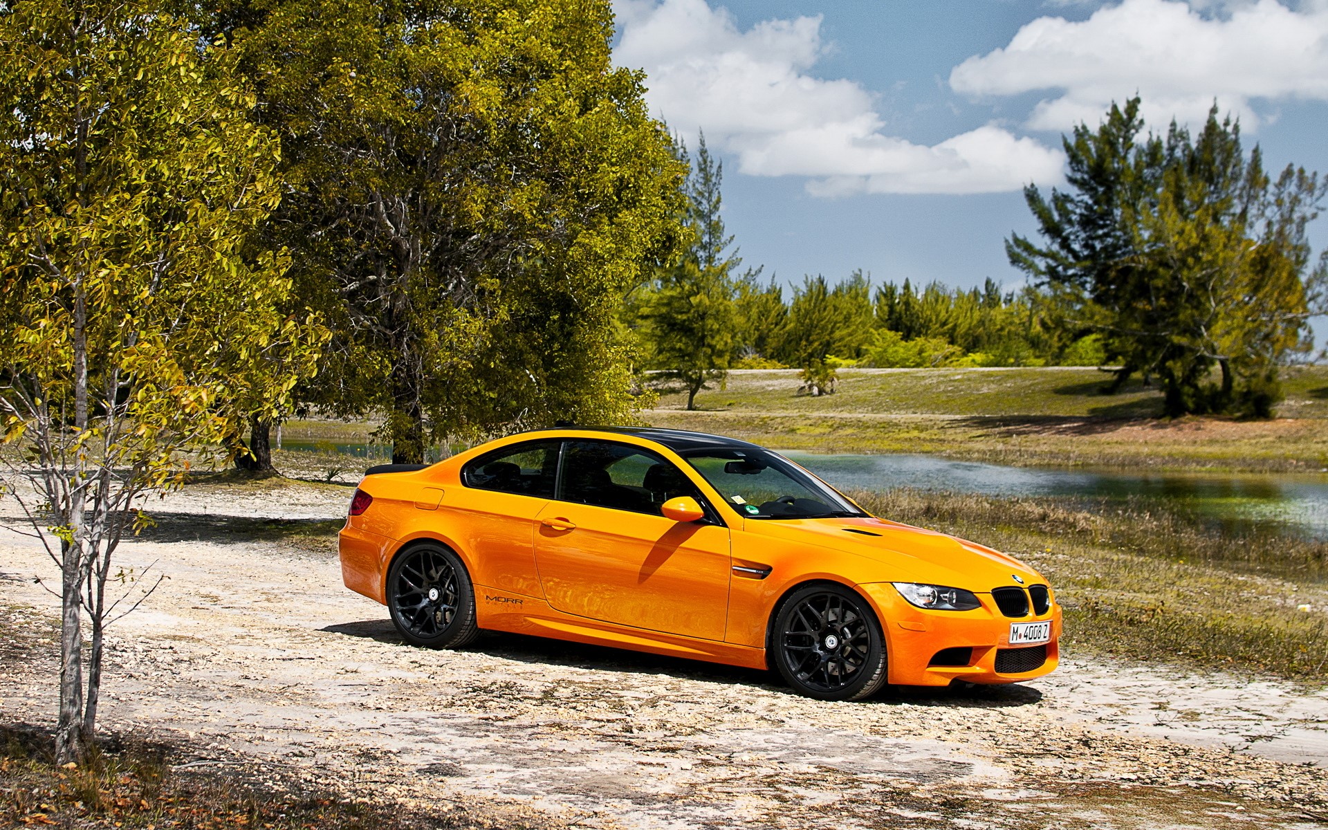 Orange BMW M3 Coupe on a dirt road HD Wallpaper