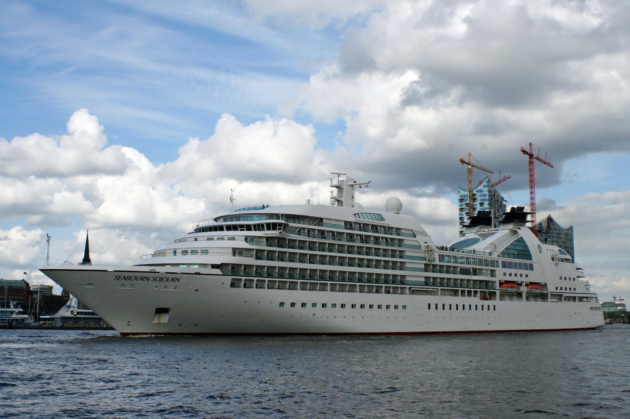 Seabourn Sojourn cruise liner sailing on water with cranes and buildings in background HD Wallpaper