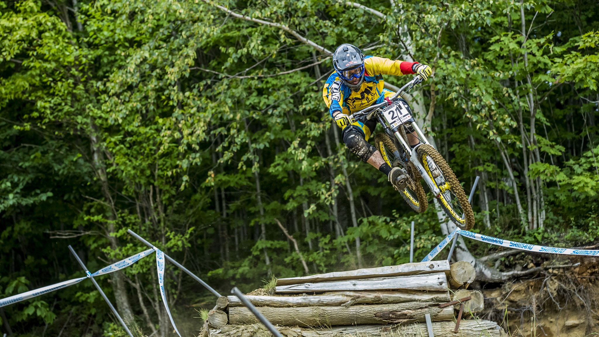 Downhill mountain biker jumps over logs HD Wallpaper