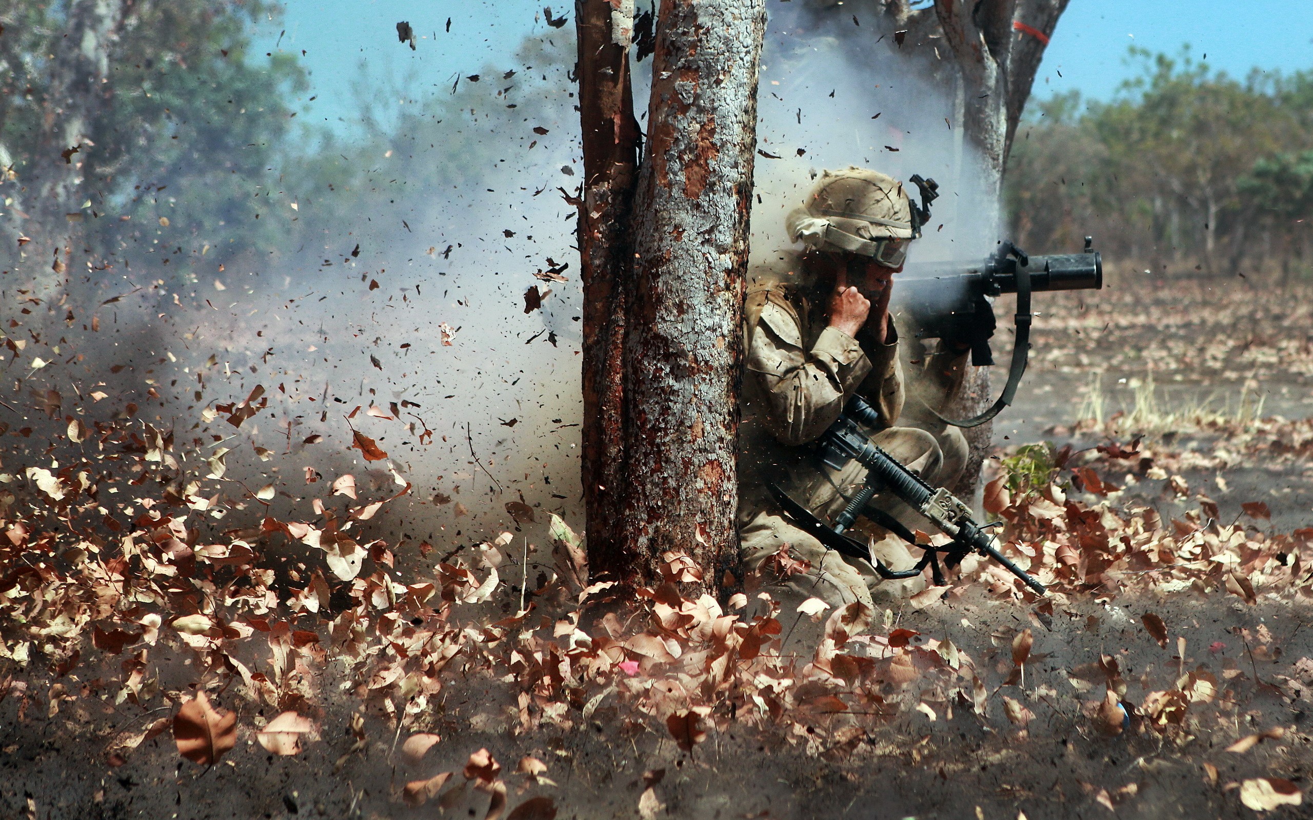 Soldier firing weapon amidst explosion and foliage HD Wallpaper