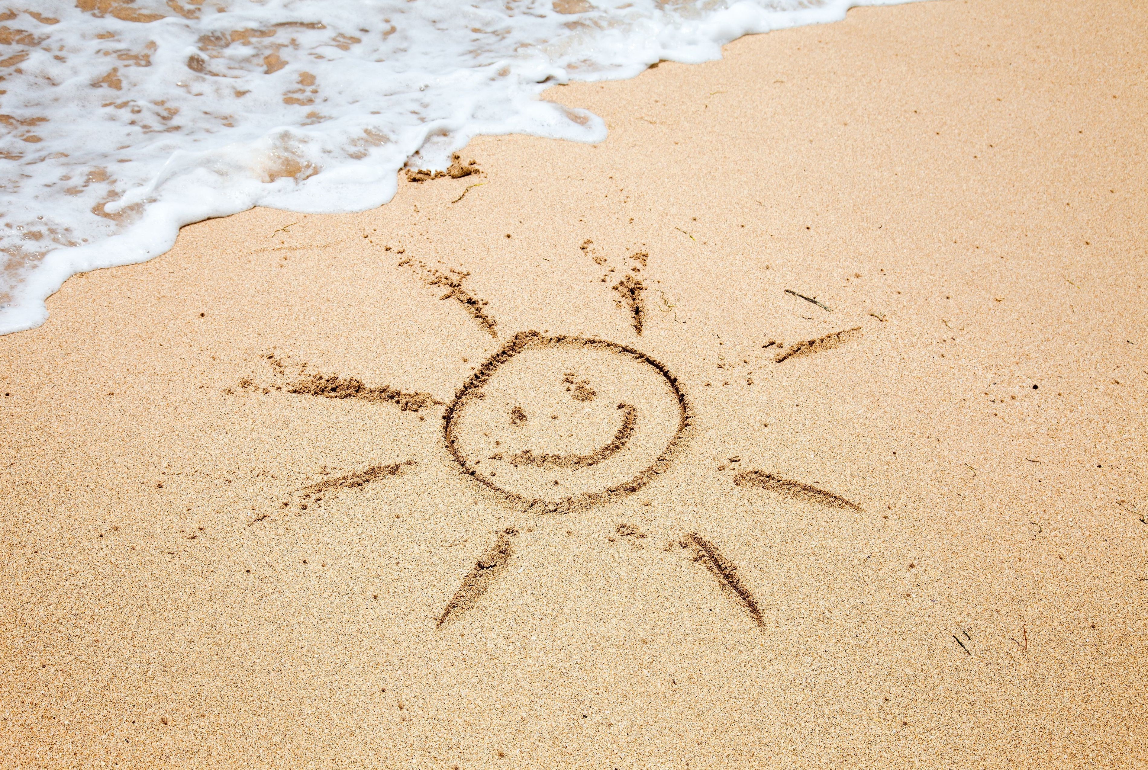 Drawing of a smiling sun in the sand at the beach HD Wallpaper