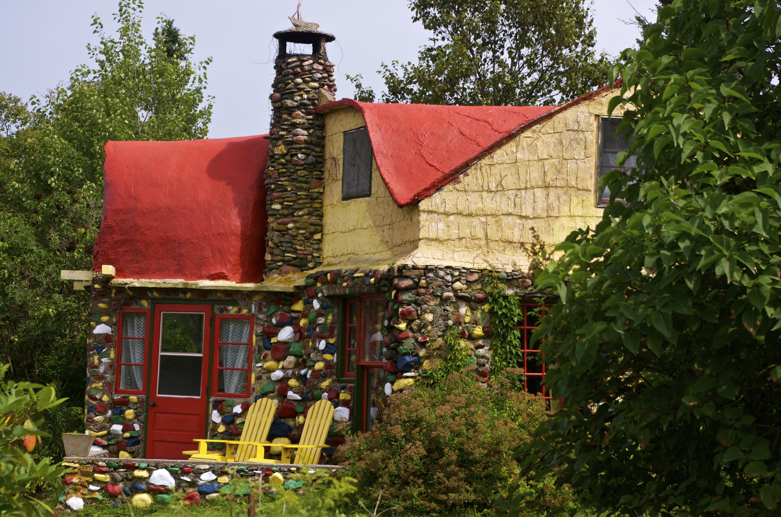 Quirky stone house with red roof and yellow chairs HD Wallpaper
